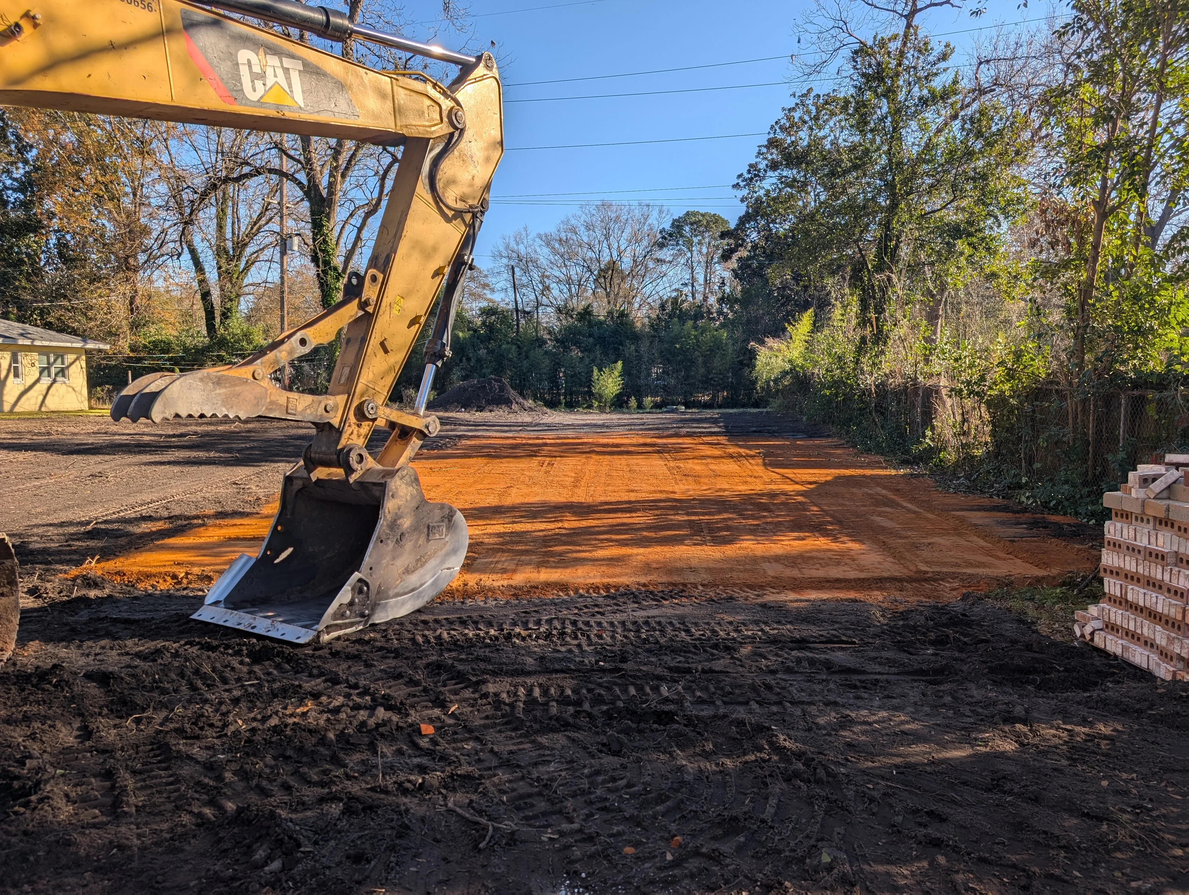 CAT excavator with bucket on residential lot showing excavated soil and prepared grading