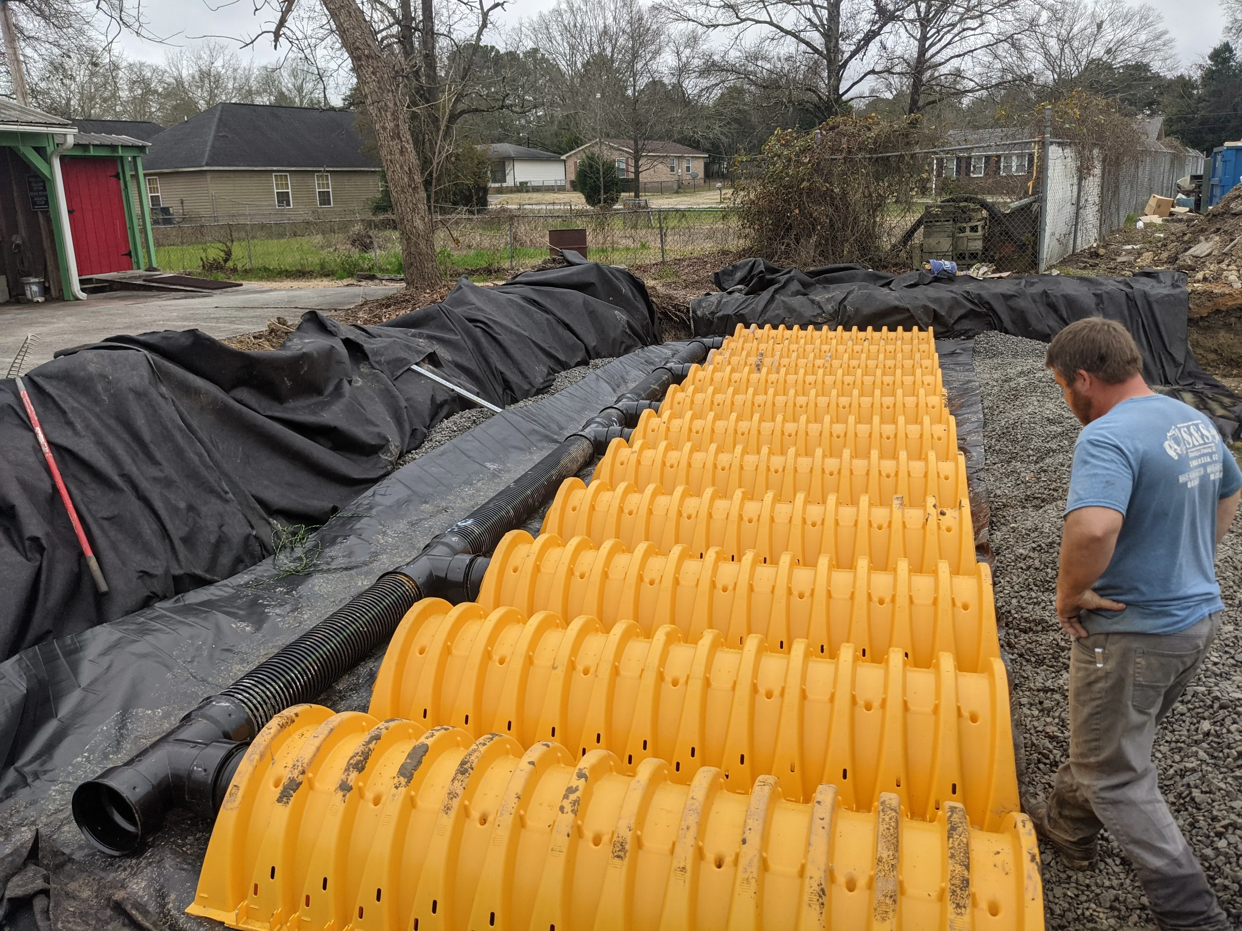 Yellow corrugated drain pipe and black landscape fabric drainage system installation with gravel base