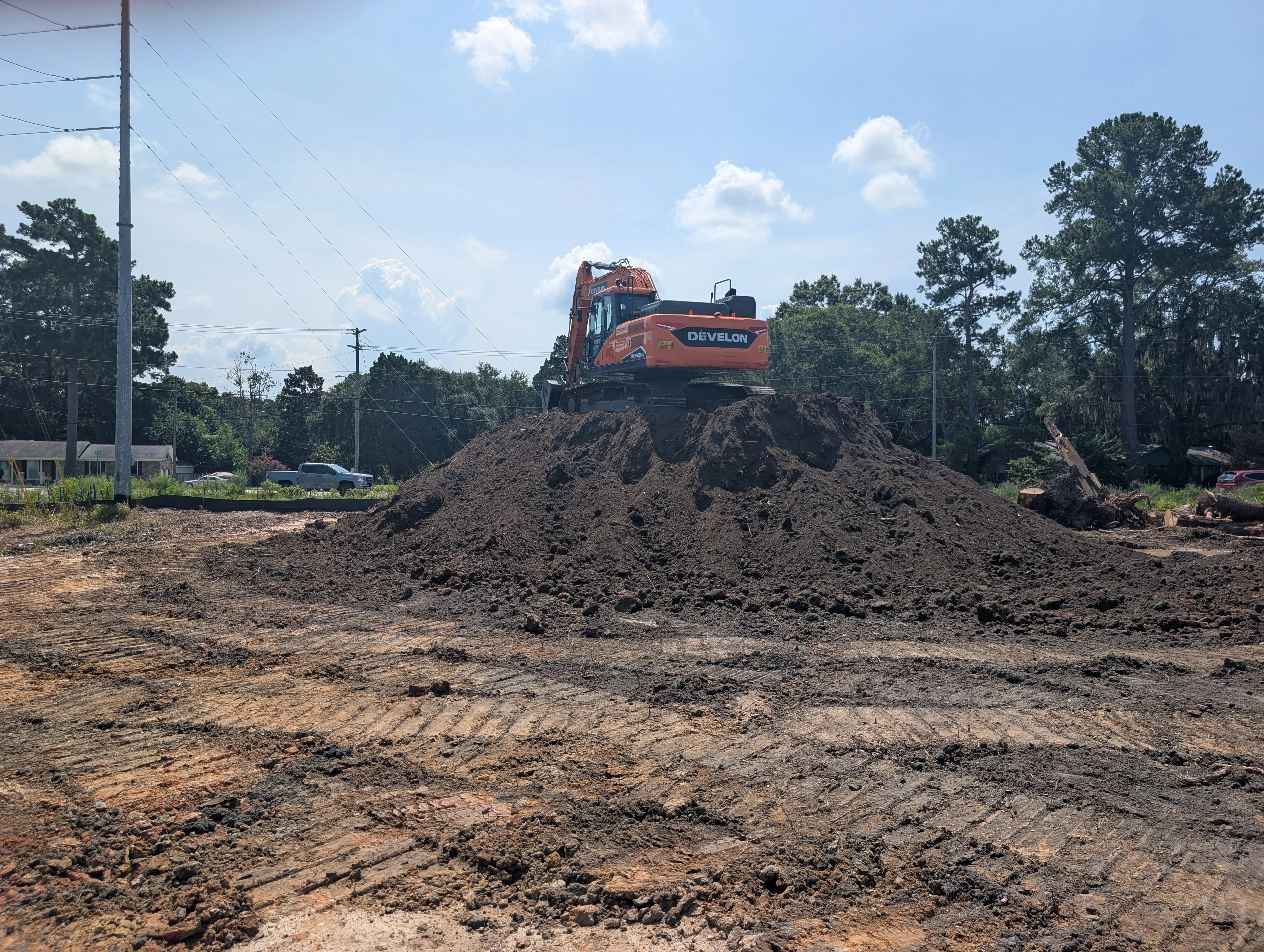 Tracked excavator on large dirt stockpile at active excavation site