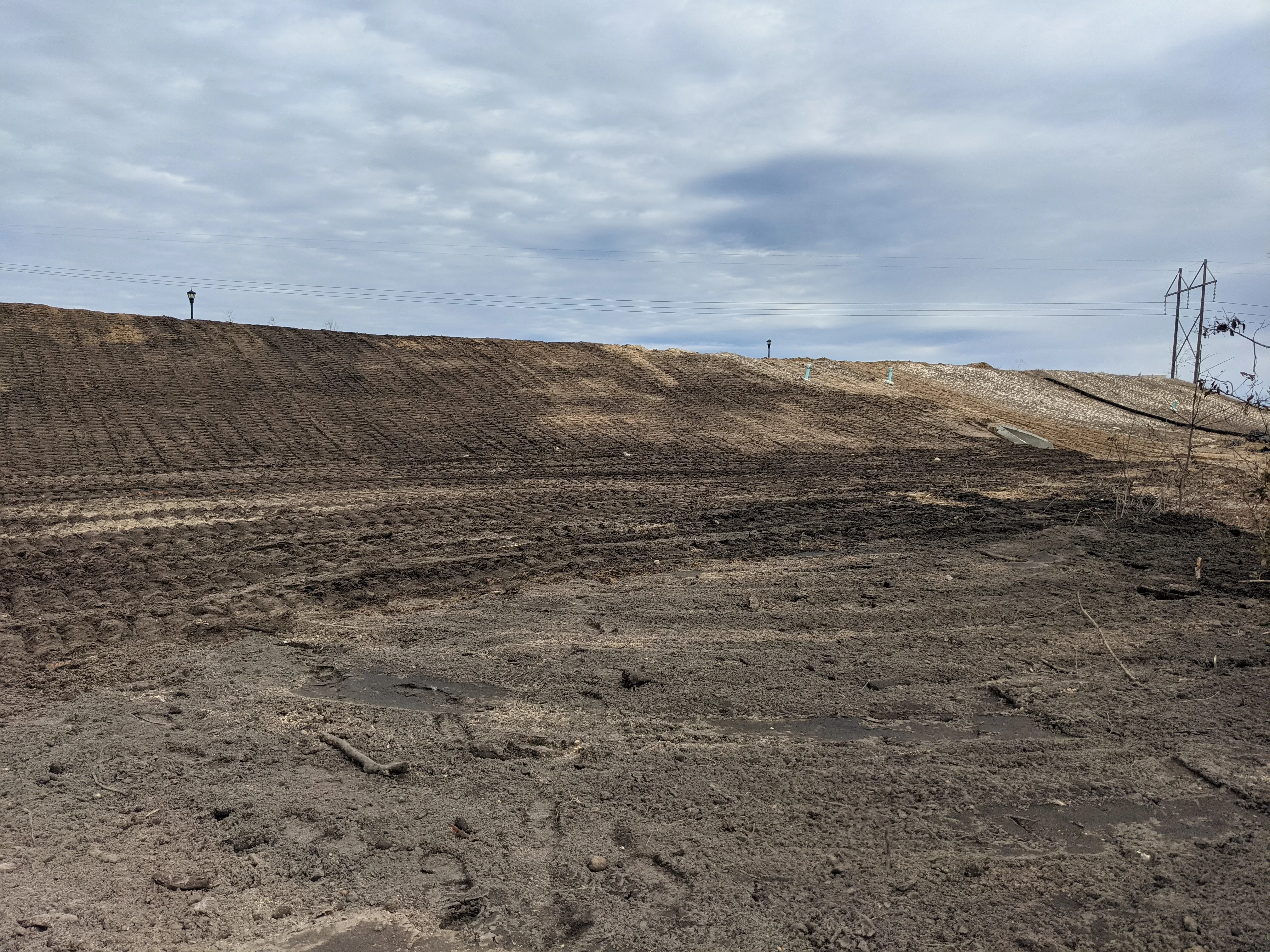 Graded dirt site with sloped earthwork, compacted soil, and utility poles