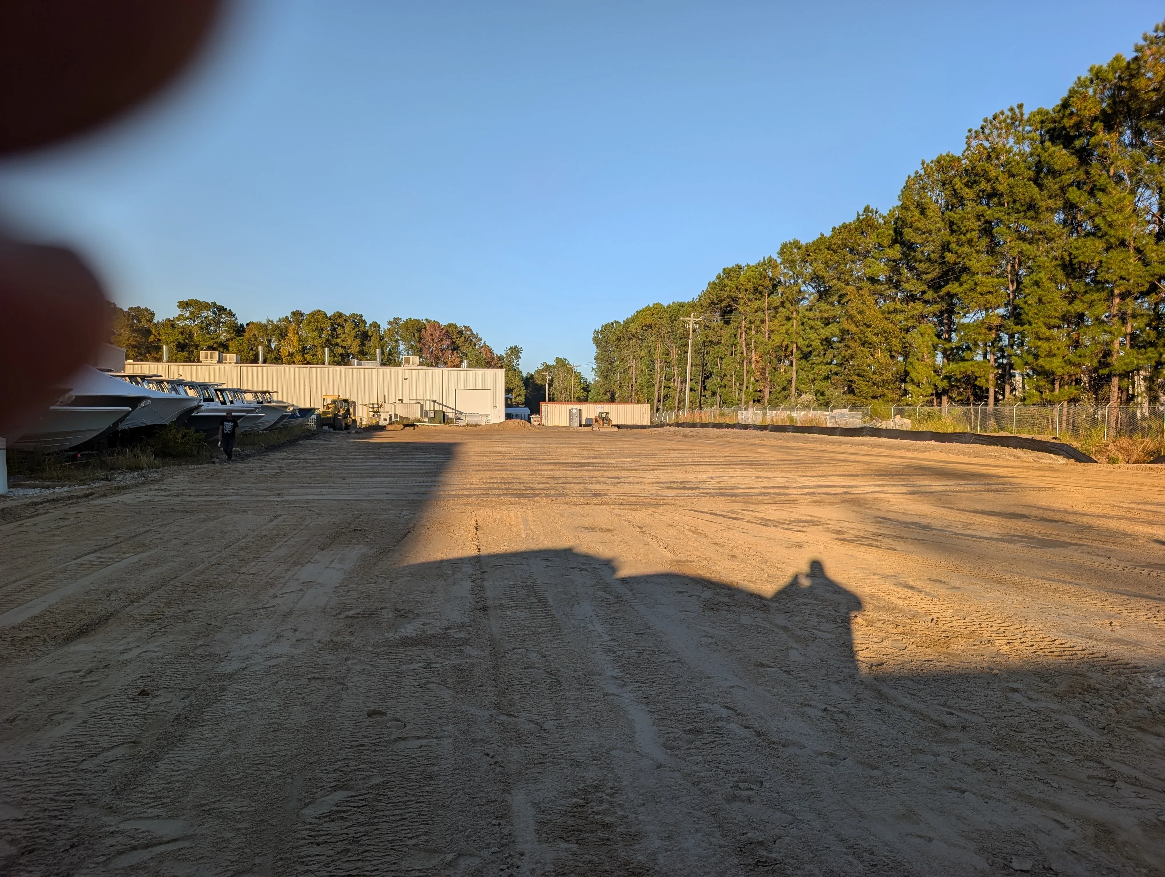 Graded dirt lot with metal industrial building, compacted soil surface, and cleared perimeter