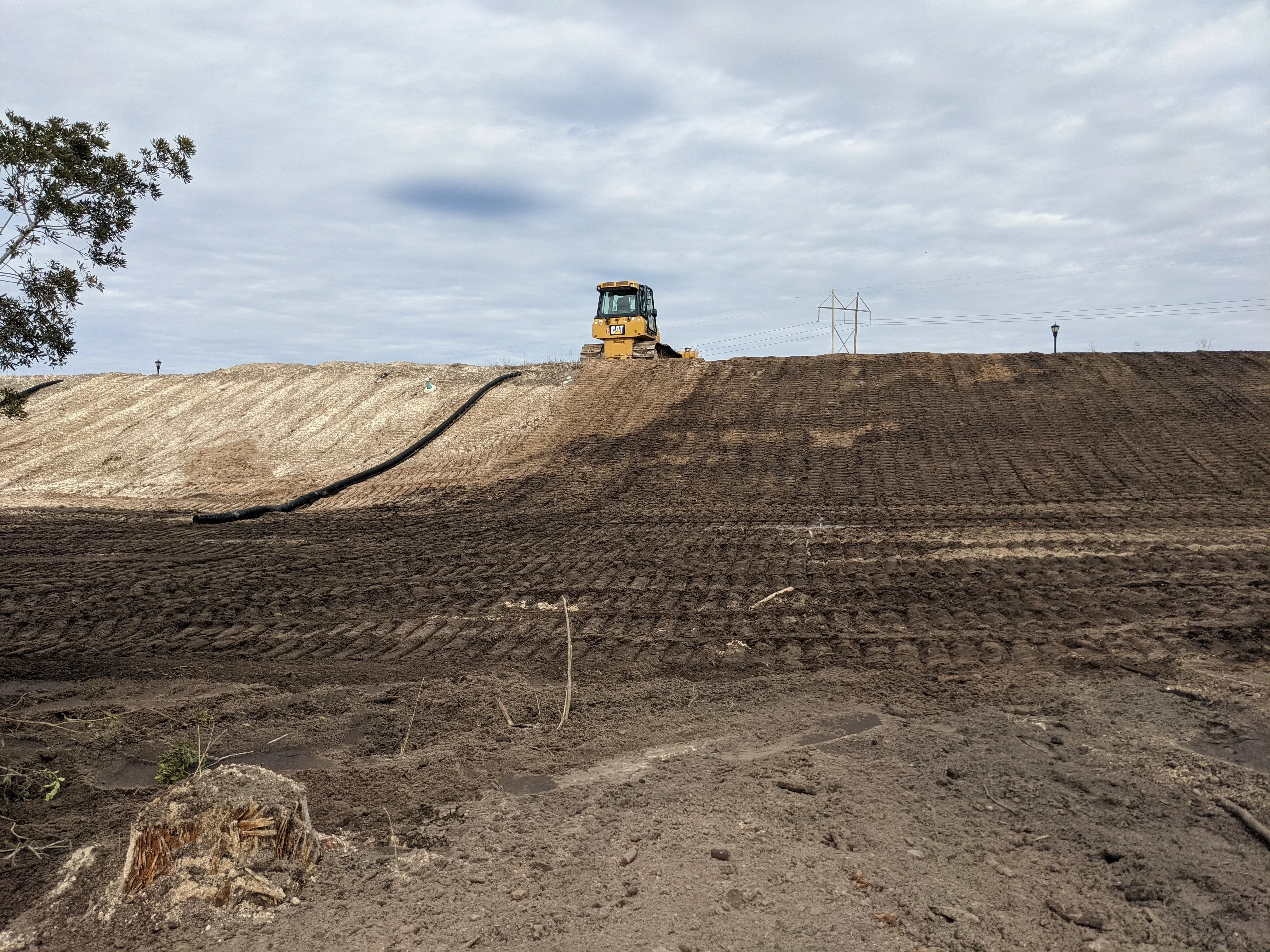 Yellow CAT dozer grading sloped earthwork with layered soil preparation and drainage pipe installation
