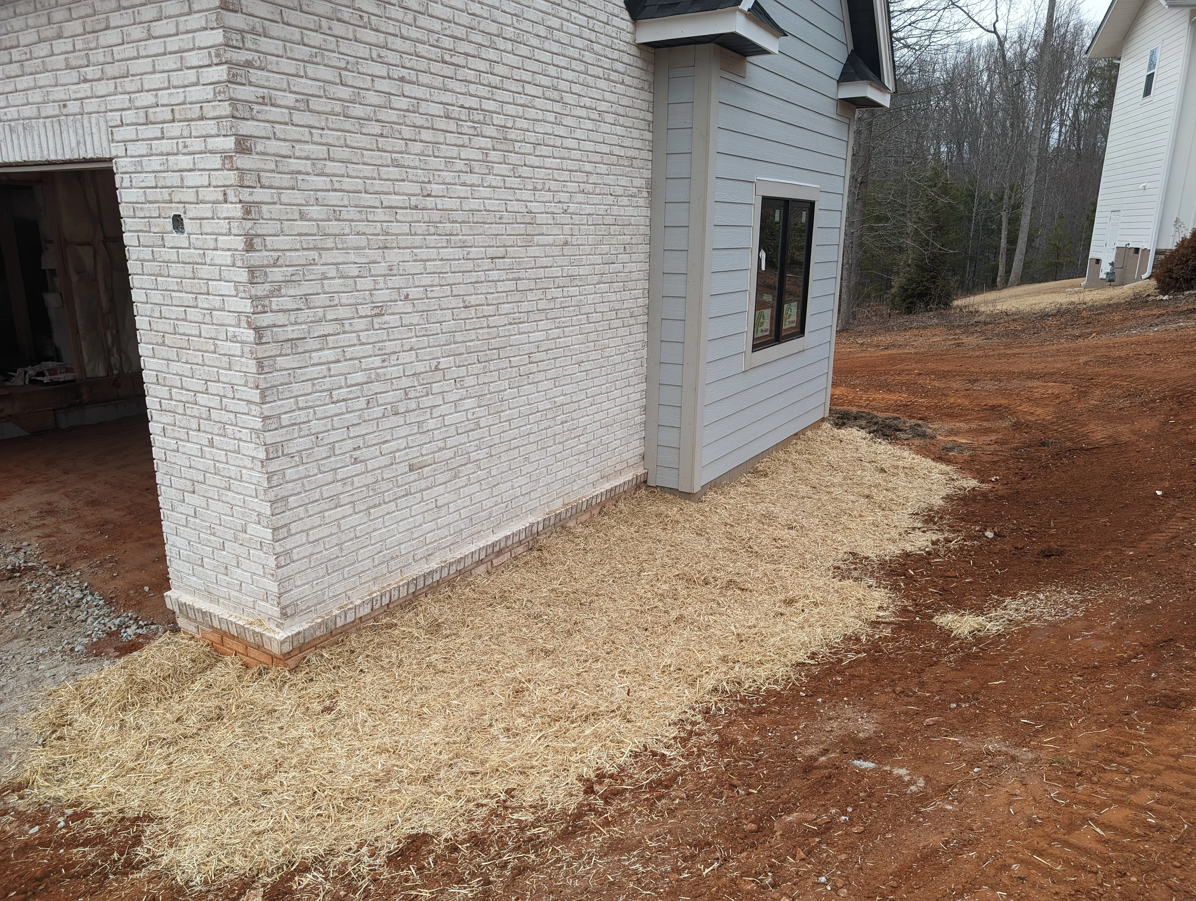 Graded residential lot with wood chip mulch base, brick foundation, and prepared drainage around new construction