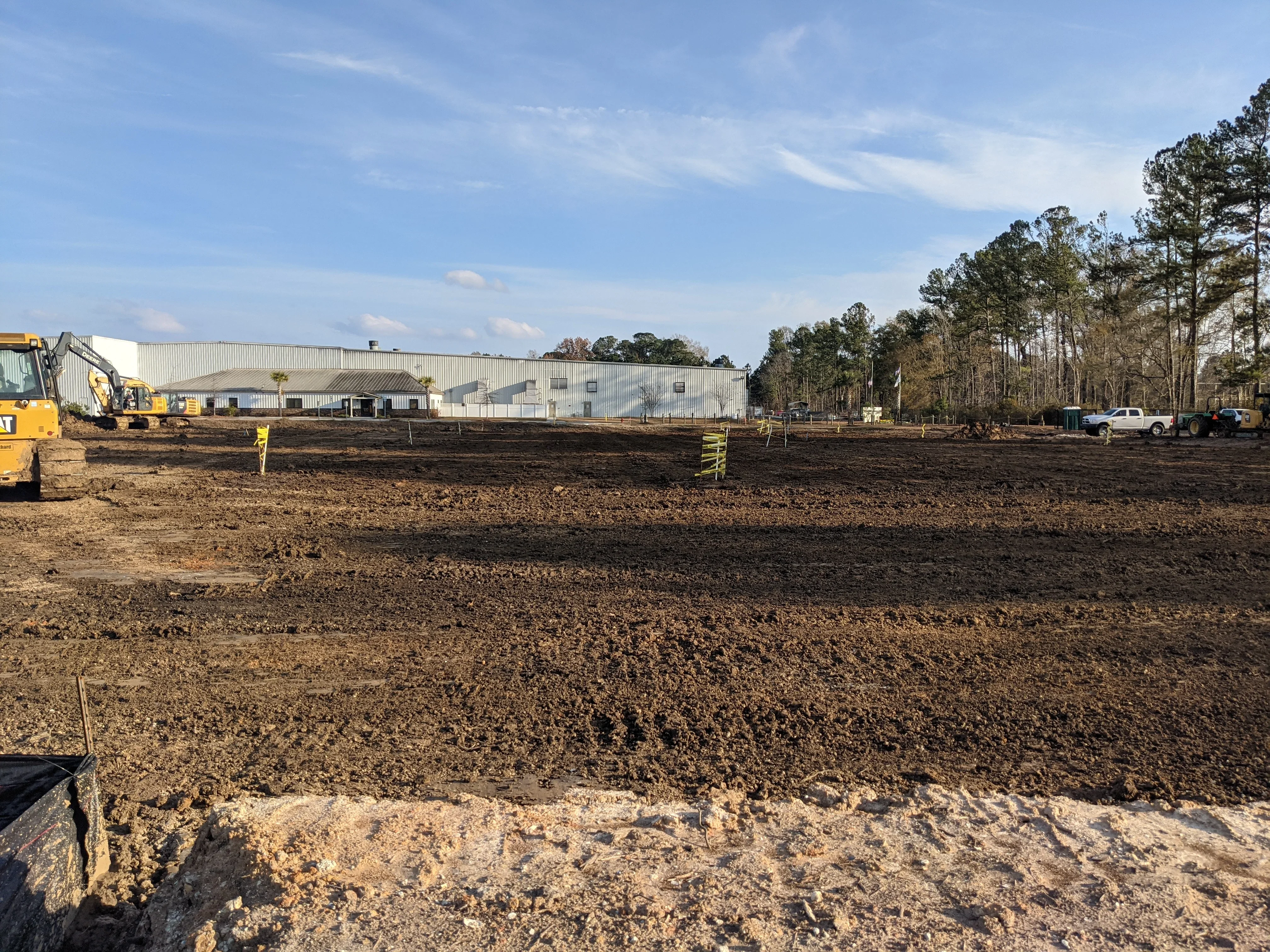 Excavated and graded commercial lot with heavy machinery and metal warehouse building