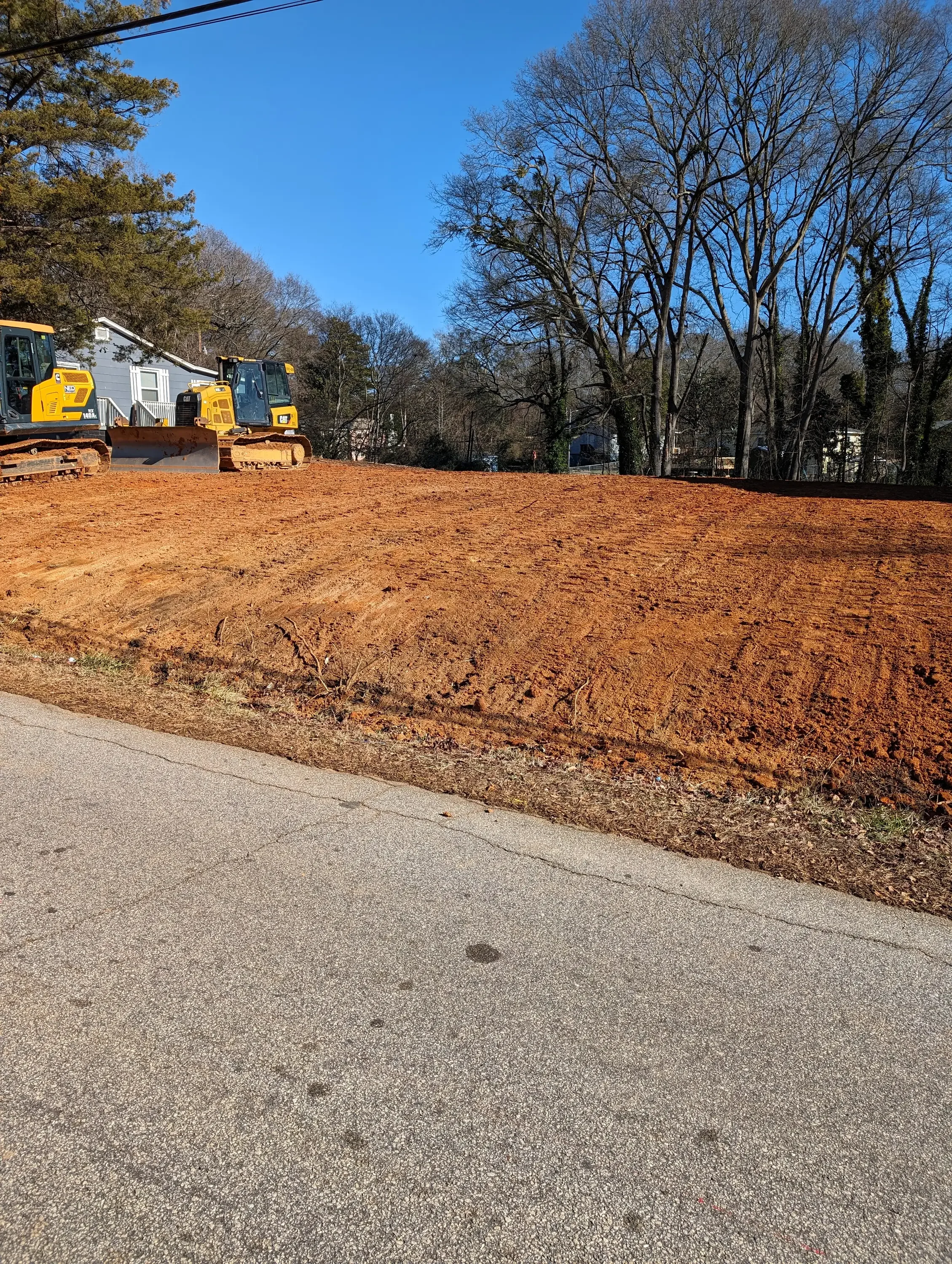 Graded residential lot with compacted soil, tracked excavator, and site preparation work