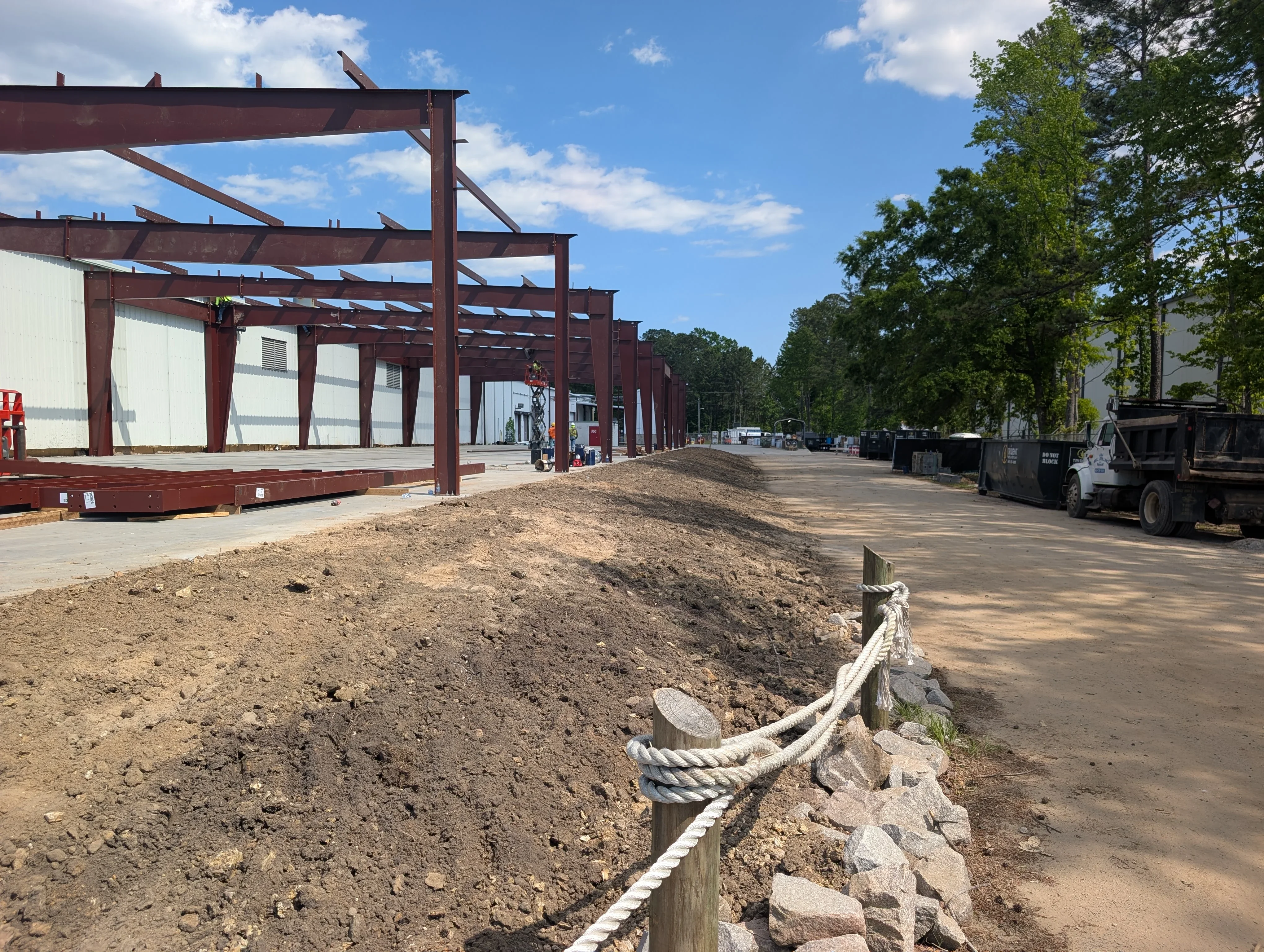 Excavated dirt pile with rope erosion control barrier, steel industrial building frame in background