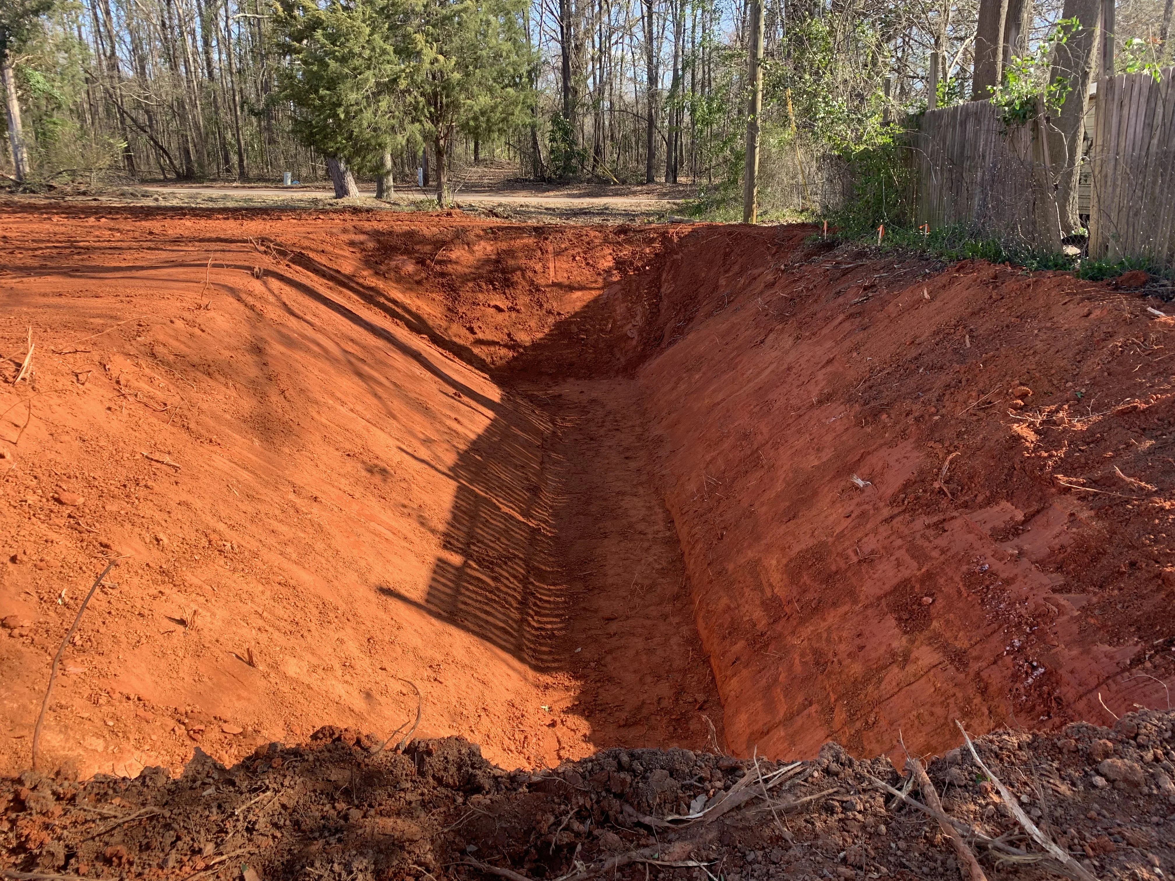 Deep excavation trench with graded soil banks on wooded residential property