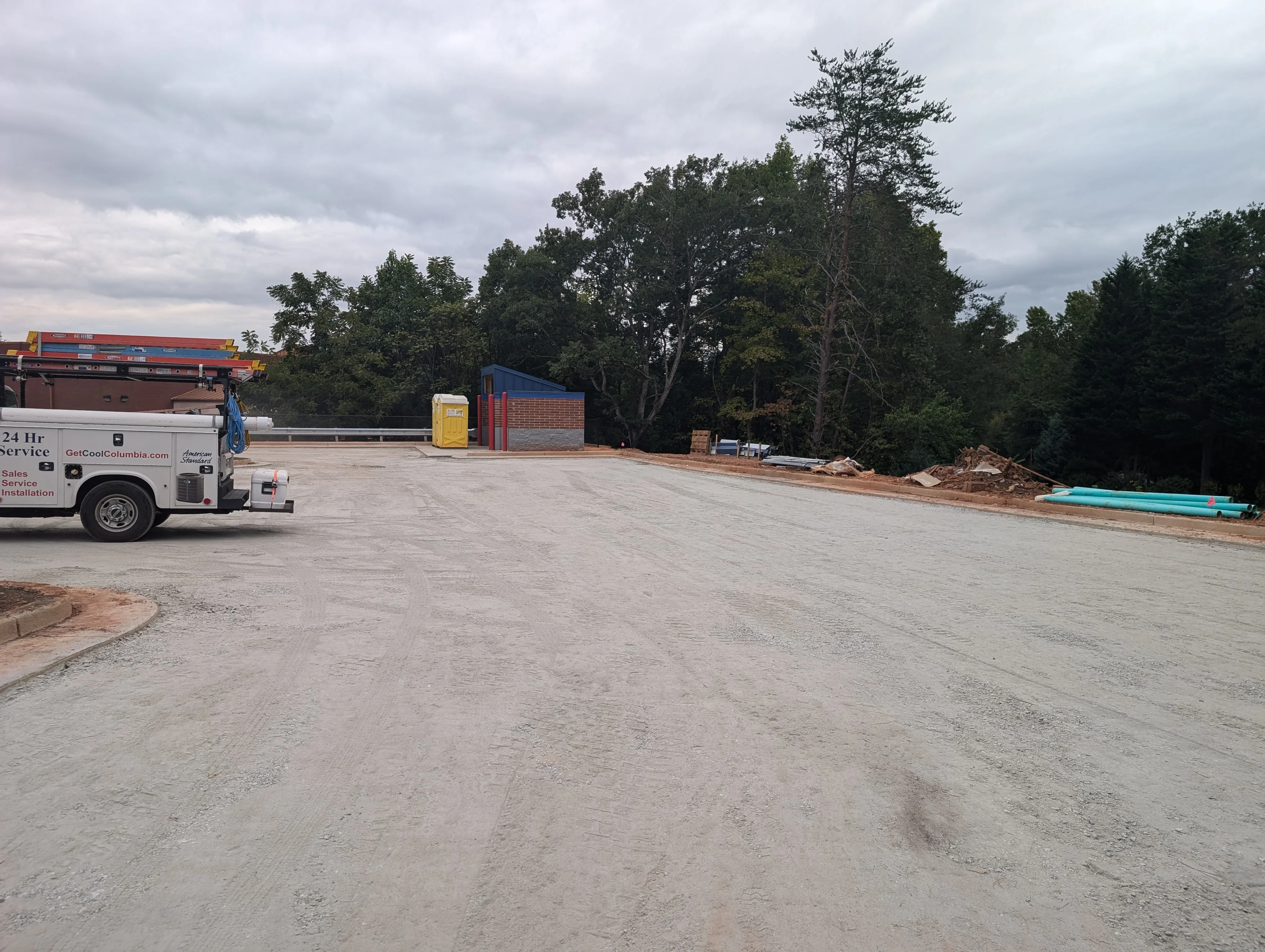 Graded commercial lot with compacted earth surface, service vehicle, and brick building structures