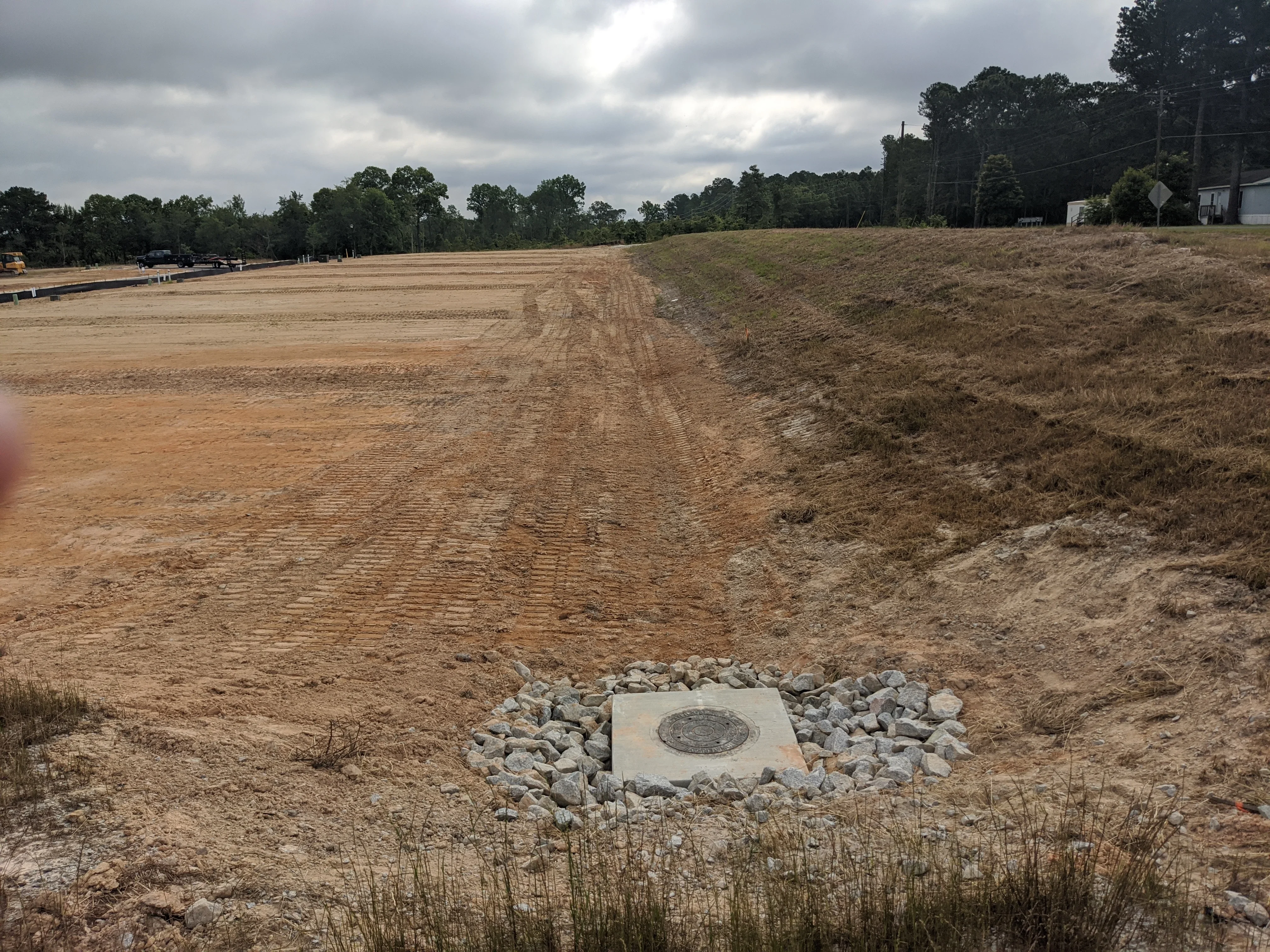 Graded dirt site with concrete drainage structure and stone base installation
