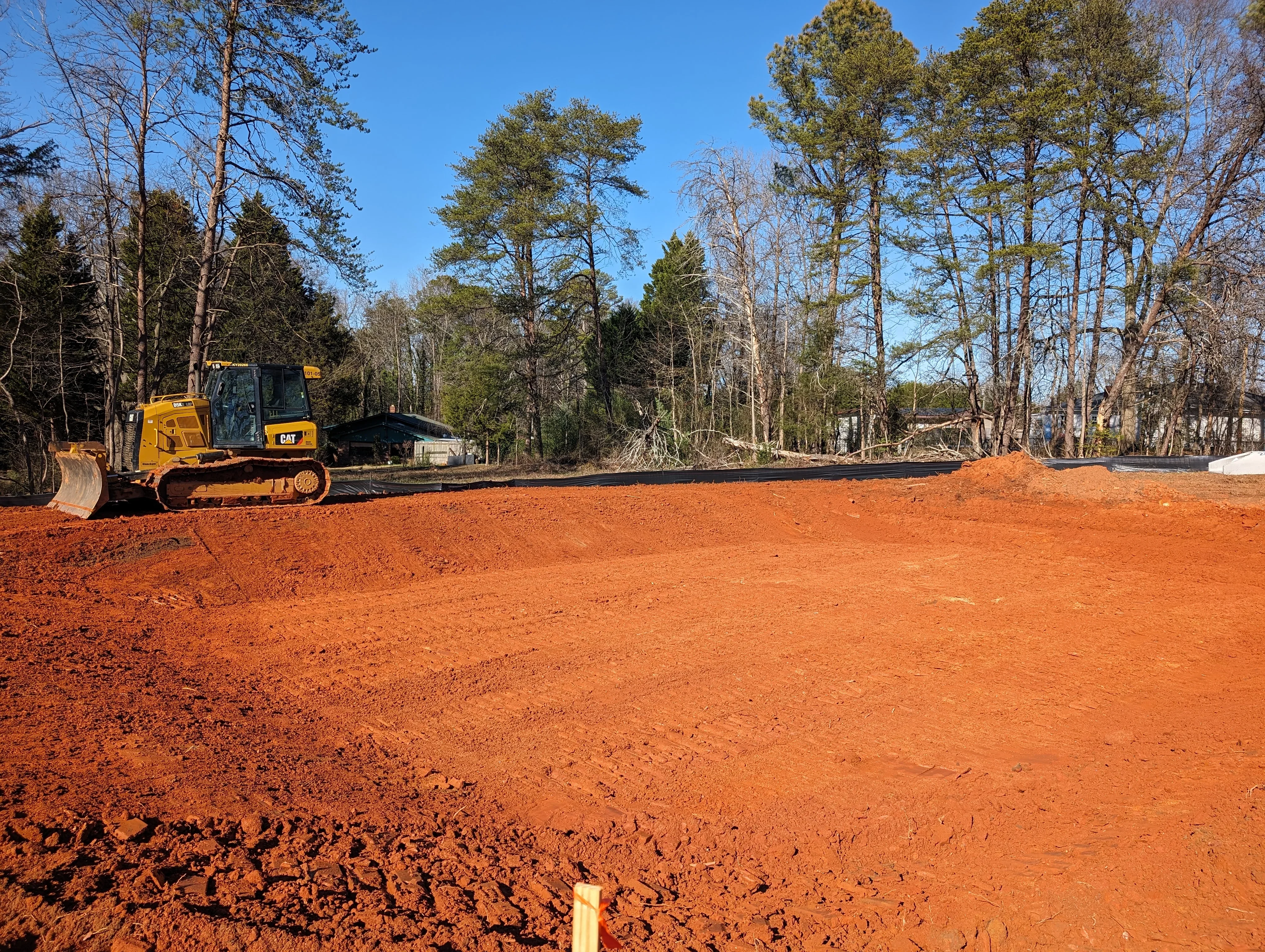 CAT bulldozer grading red clay soil on cleared wooded lot with tree removal debris