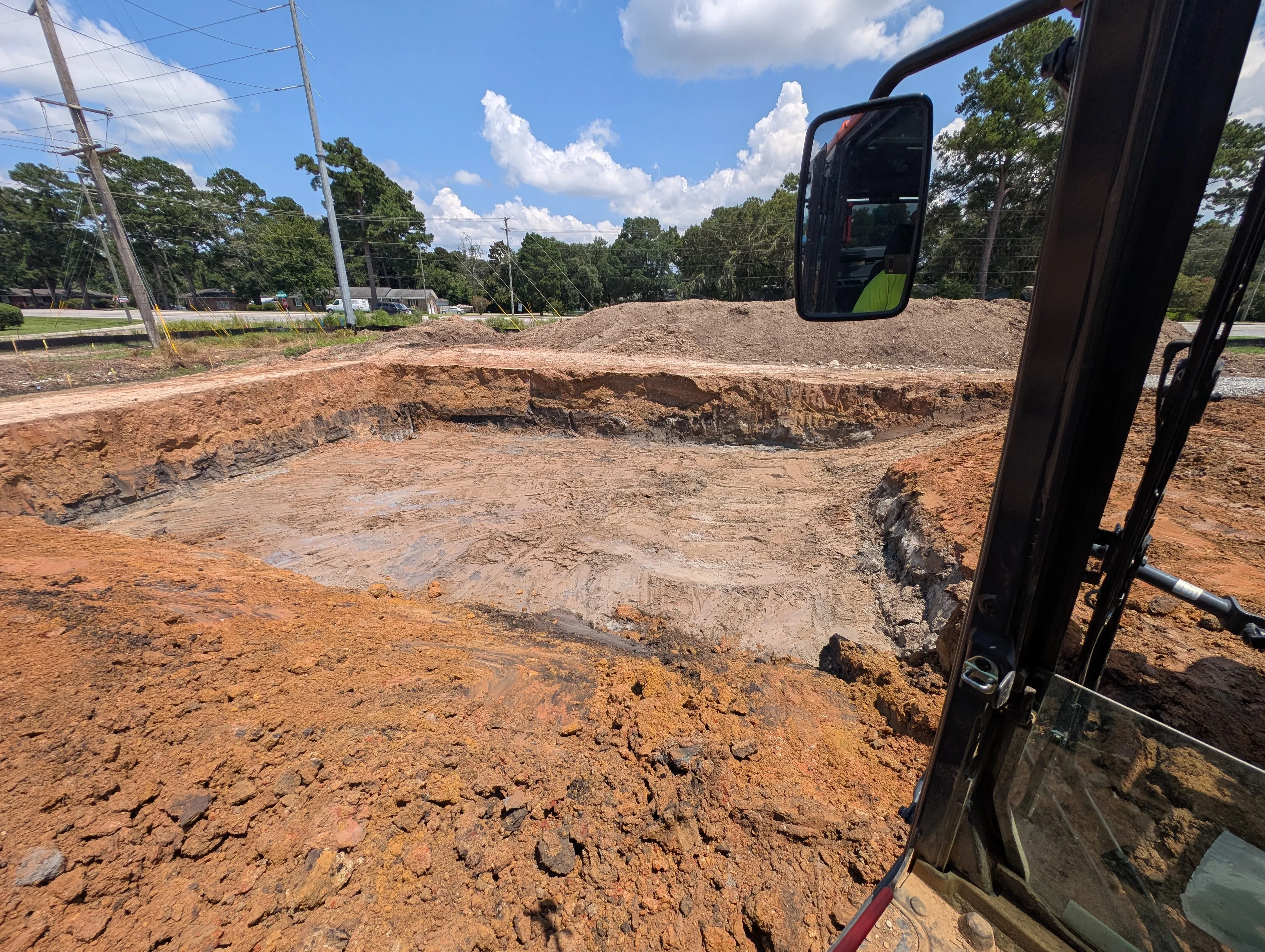 Excavated site with deep cut, staged soil piles, and heavy equipment during active grading work