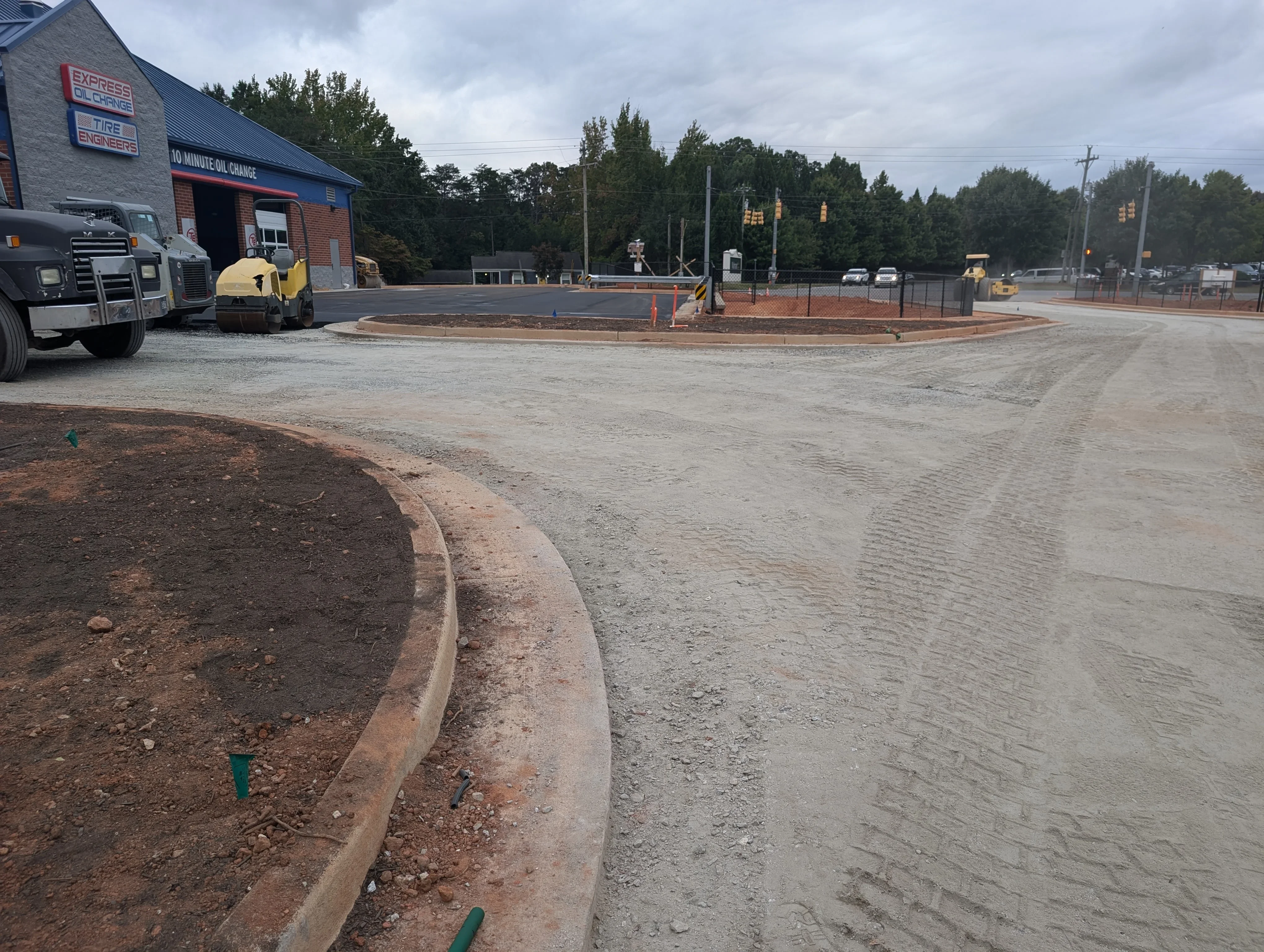 Graded commercial lot with concrete curbing, compacted base material, and metal fencing installation