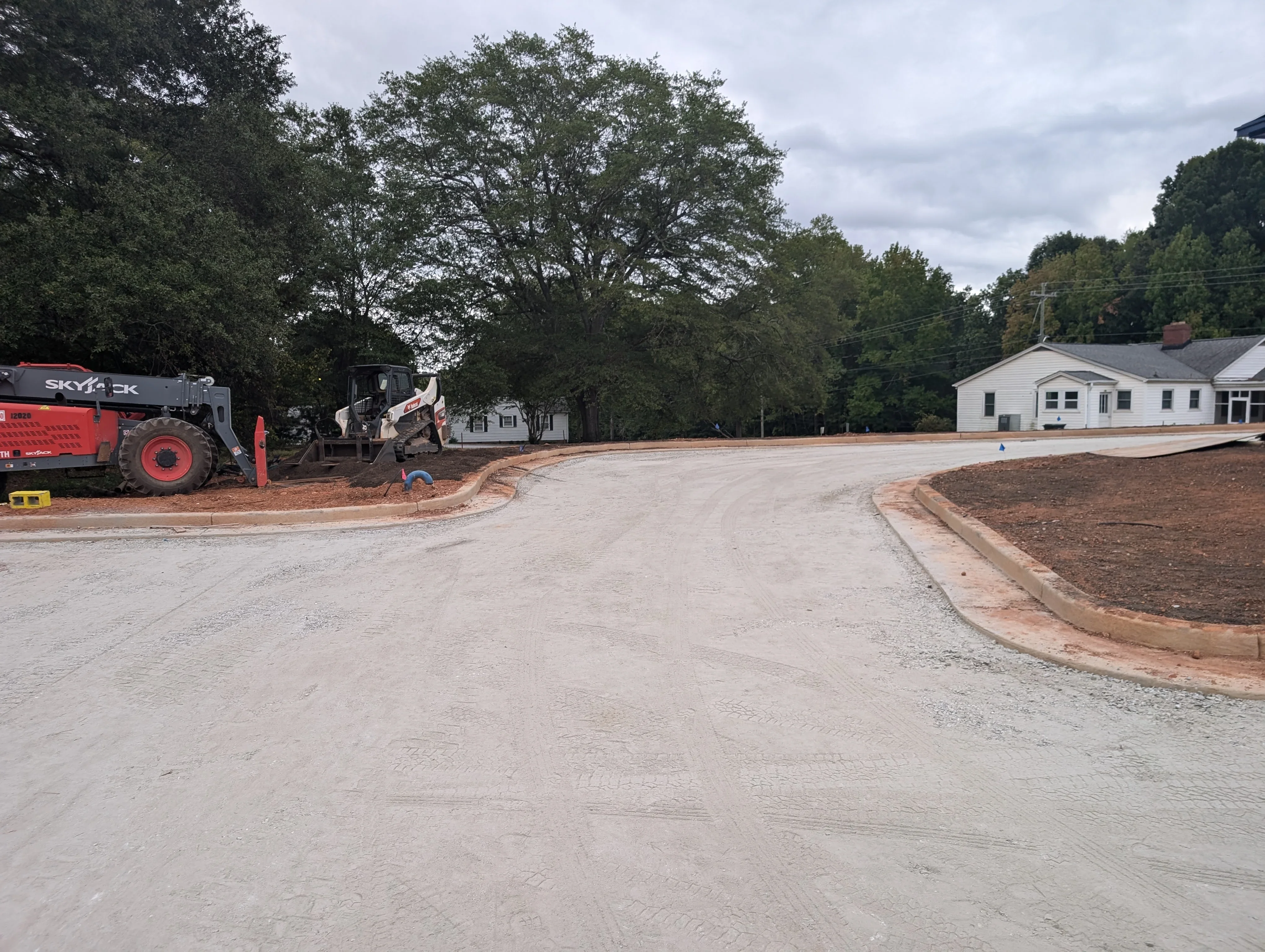 Graded driveway with compacted soil base, wooden edging, and heavy equipment on residential site