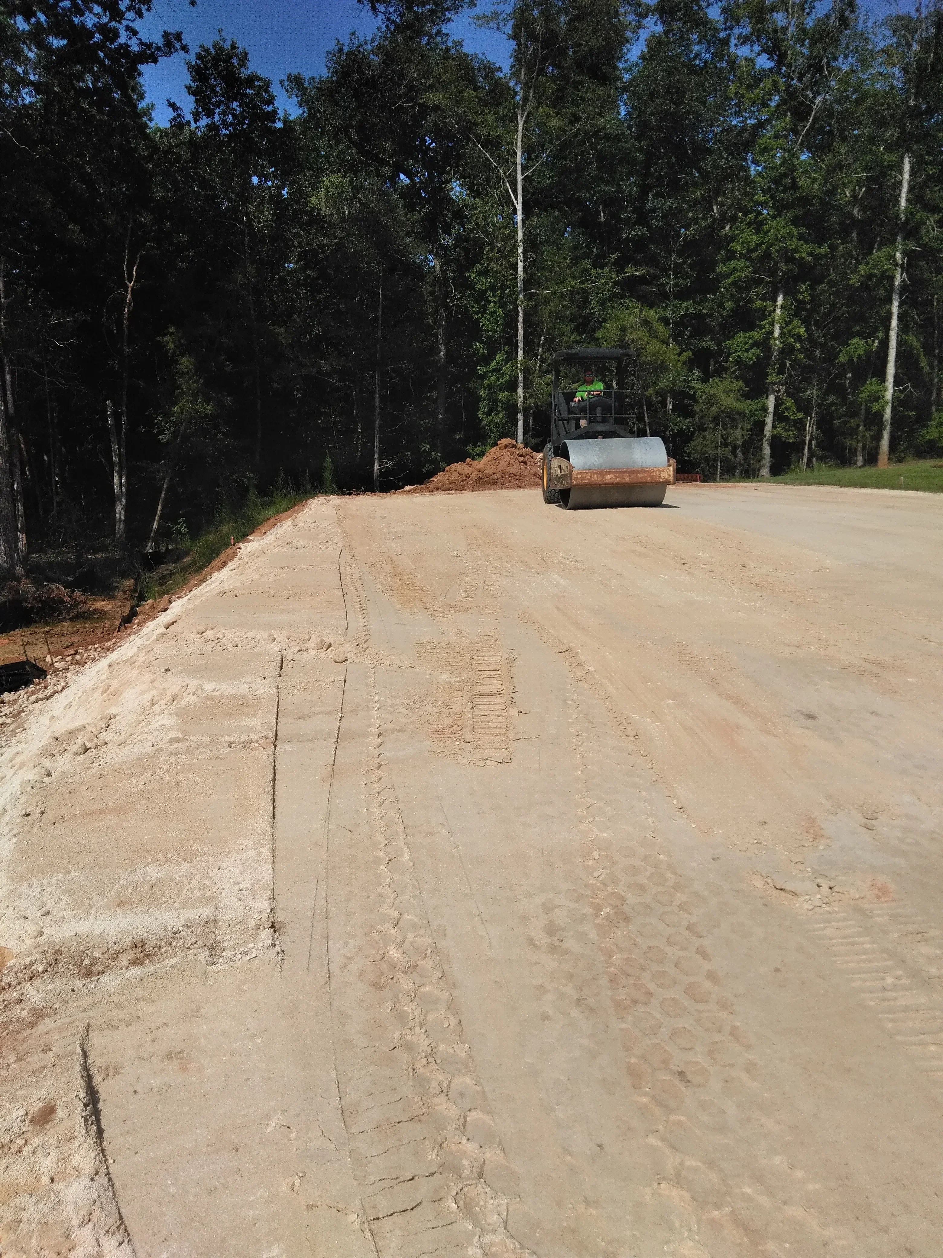 Compacted gravel driveway with roller compactor and staged material pile