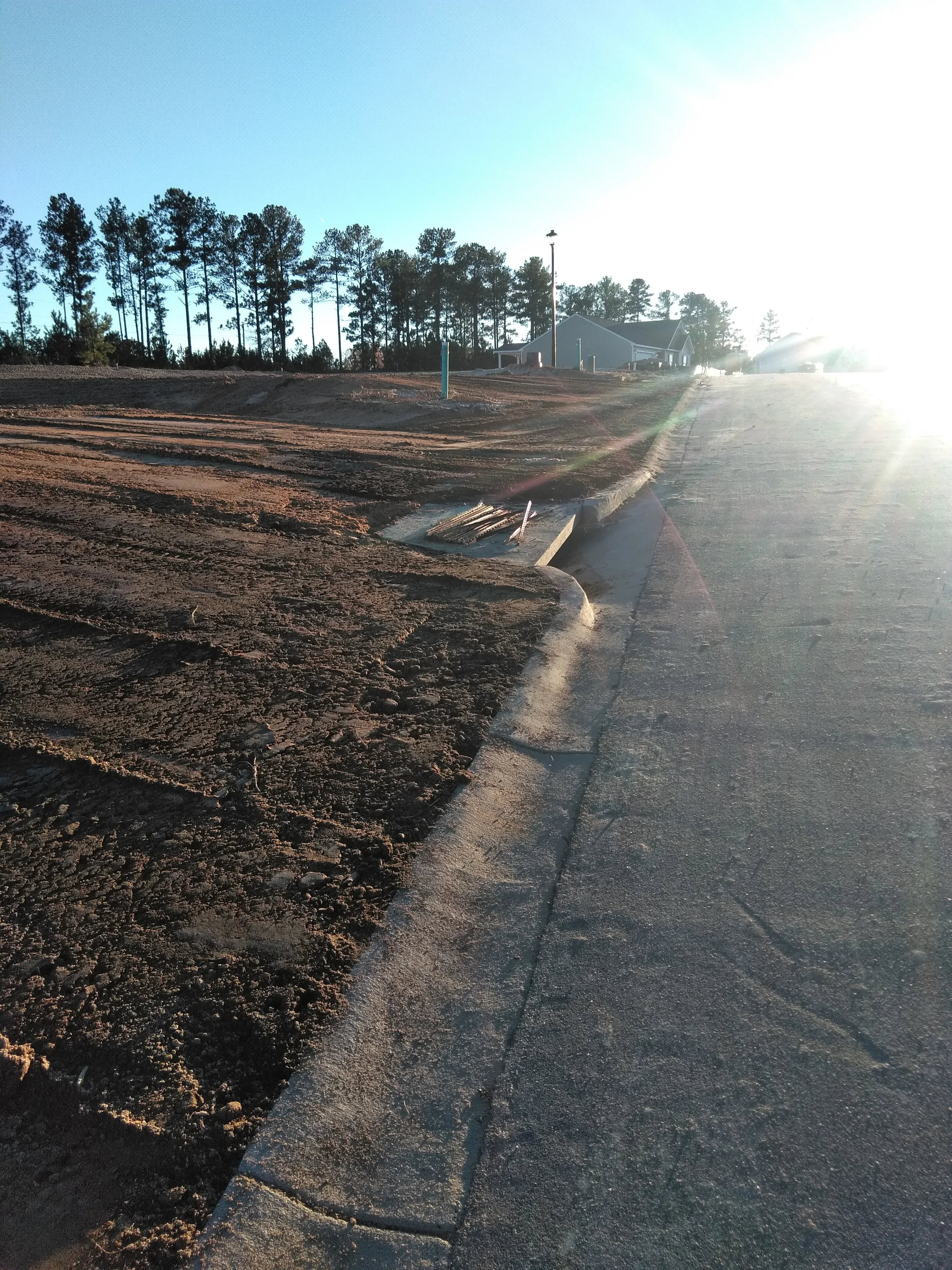 Asphalt driveway with concrete curbing and graded dirt site preparation