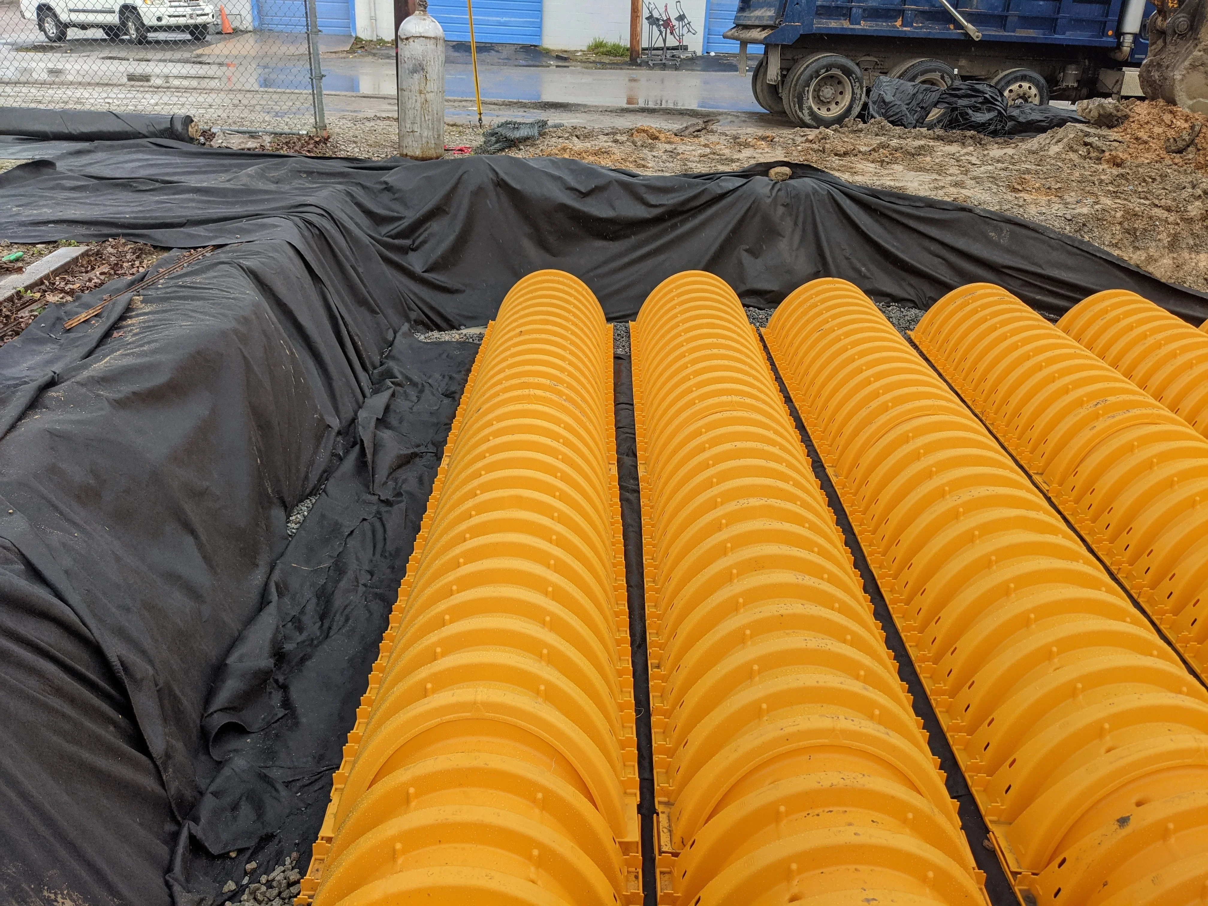 Yellow corrugated drainage pipes installed in trench with black landscape fabric