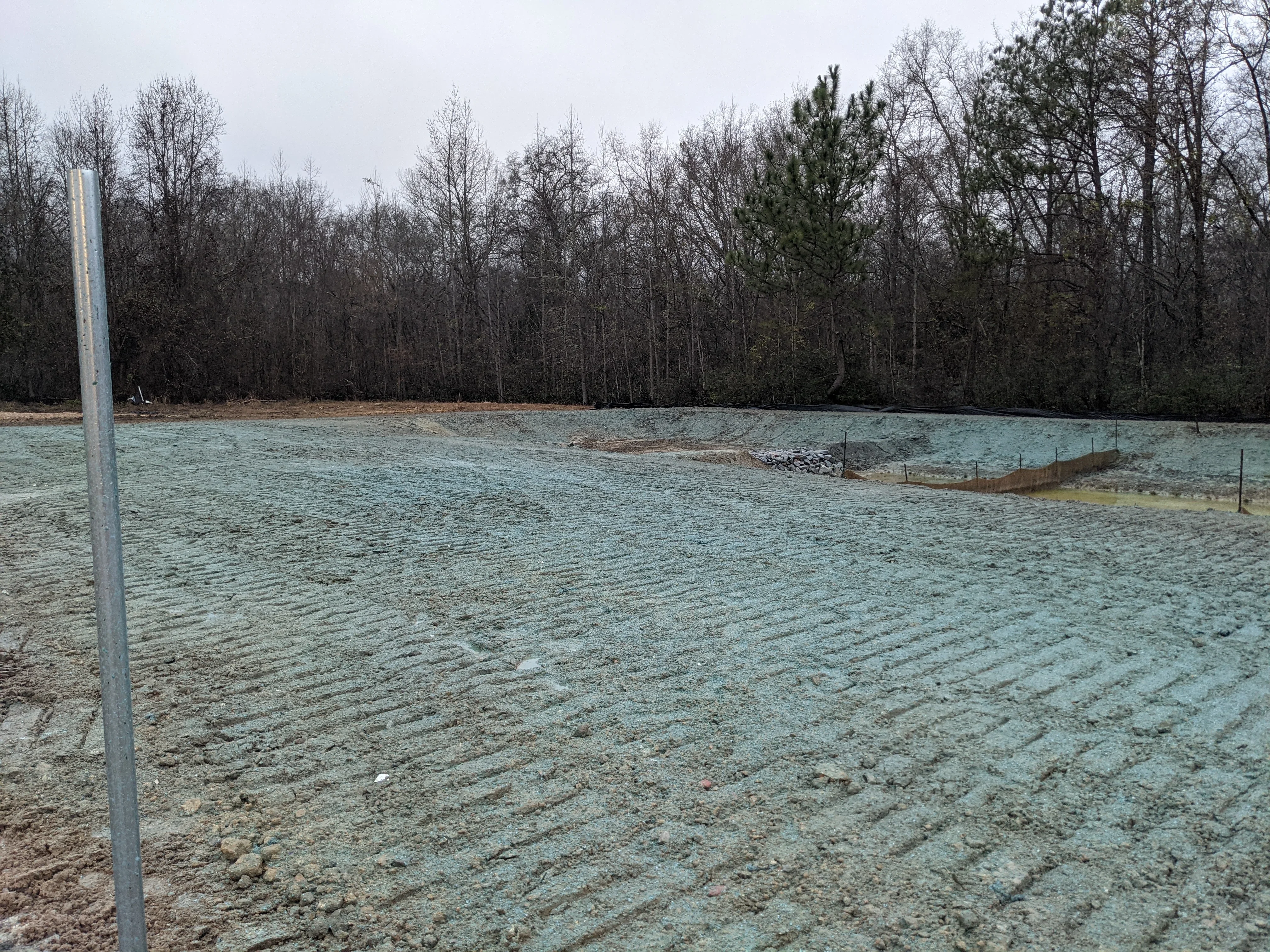 Cleared land with graded soil, erosion control fencing, and tree line backdrop