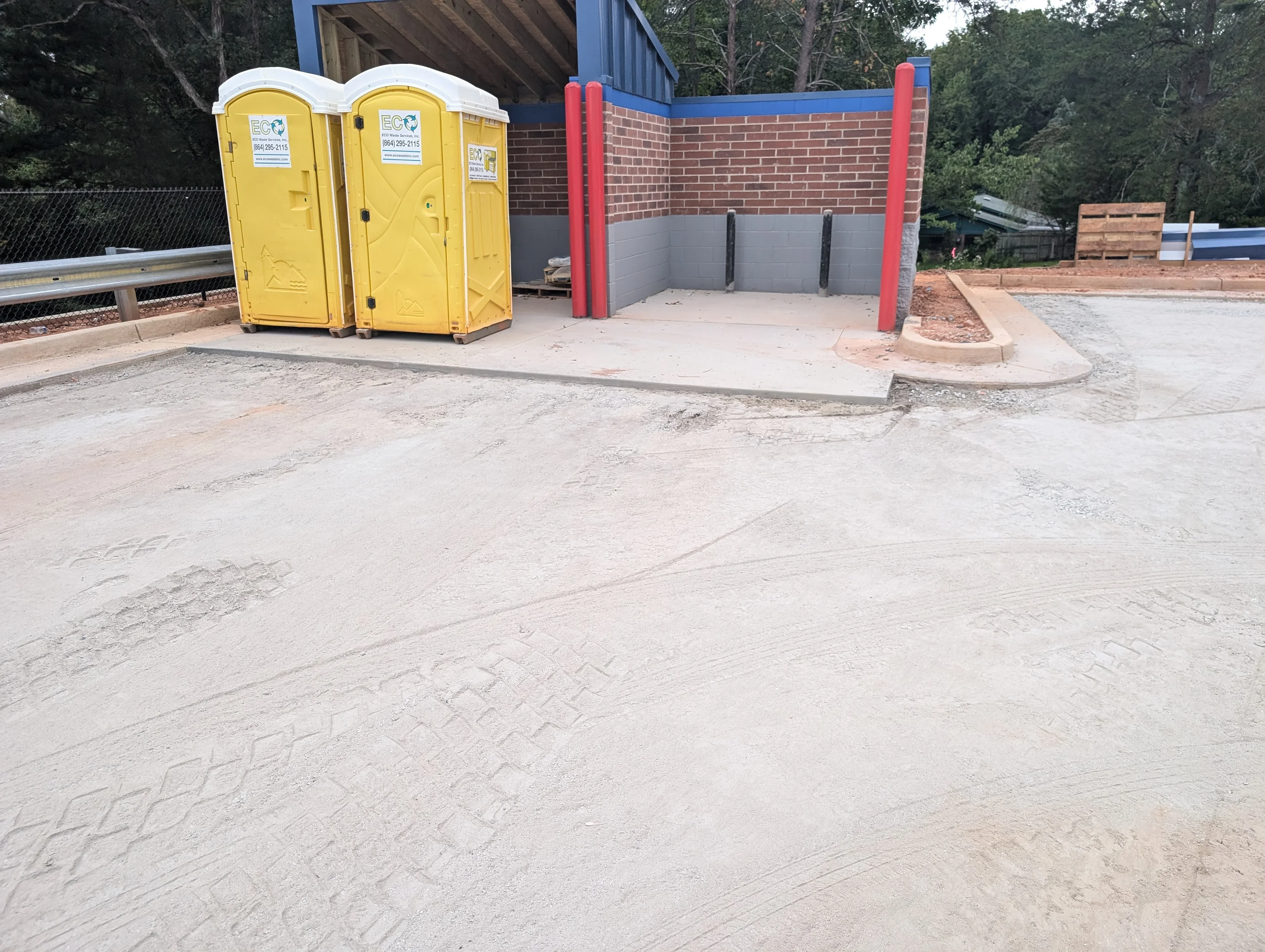 Concrete pad and graded site with brick building and red support posts