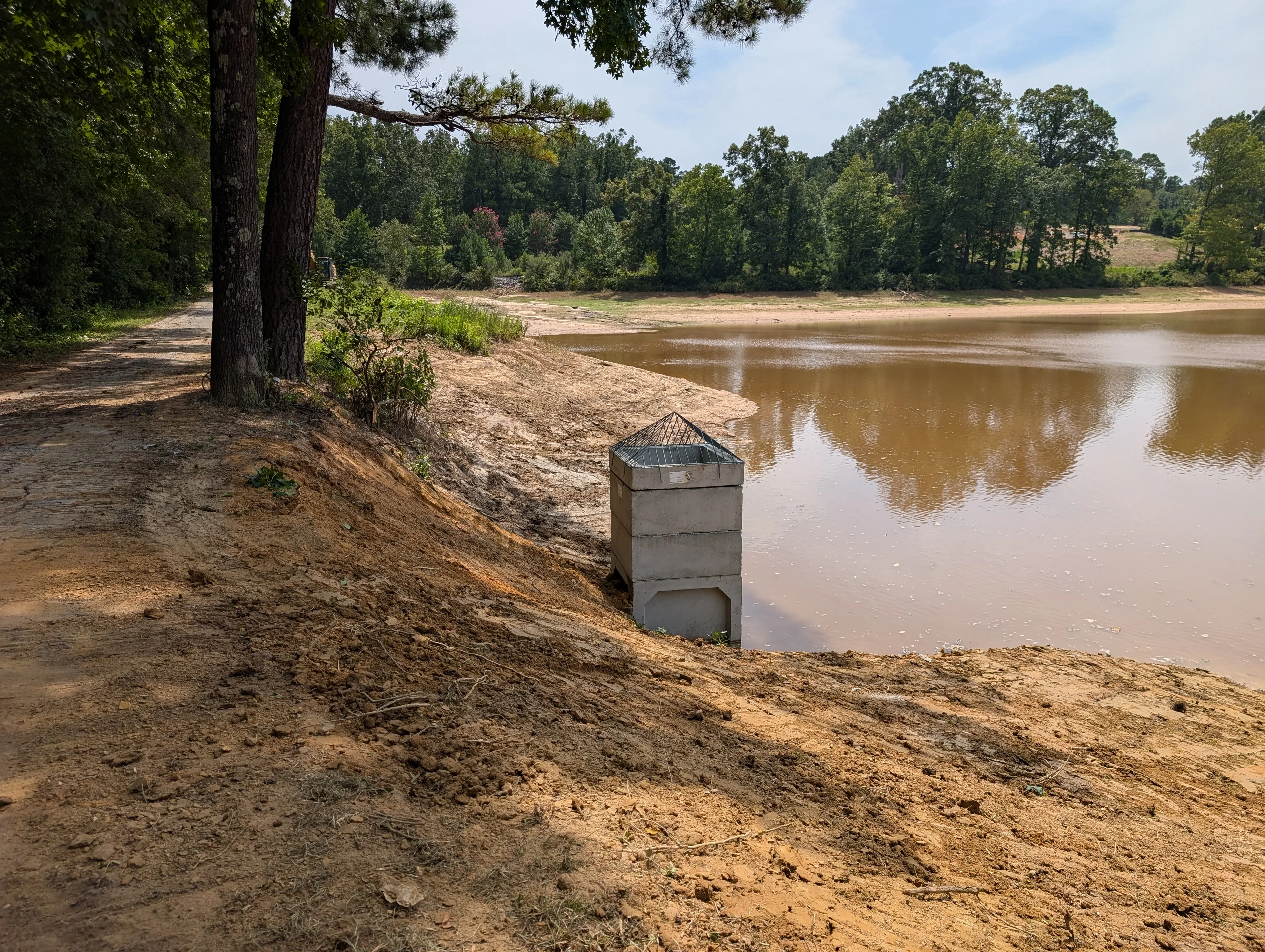 Concrete erosion control structure installed on riverbank with excavated soil and mature trees