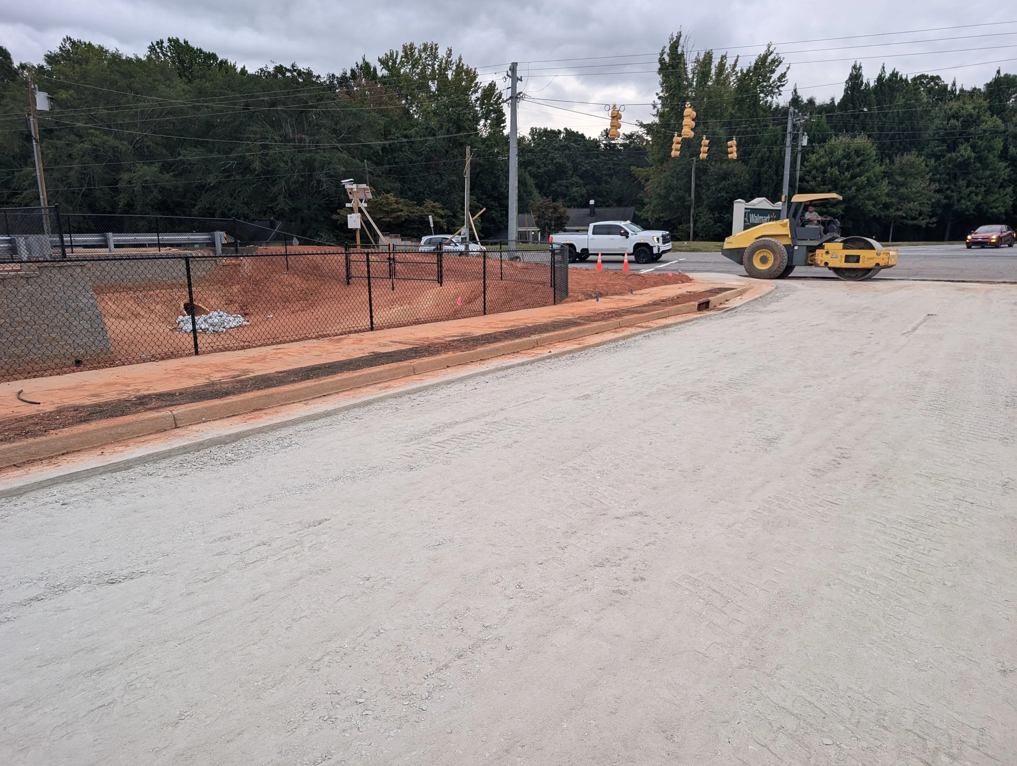 Compacted gravel lot with yellow roller compactor and chainlink fencing along property edge
