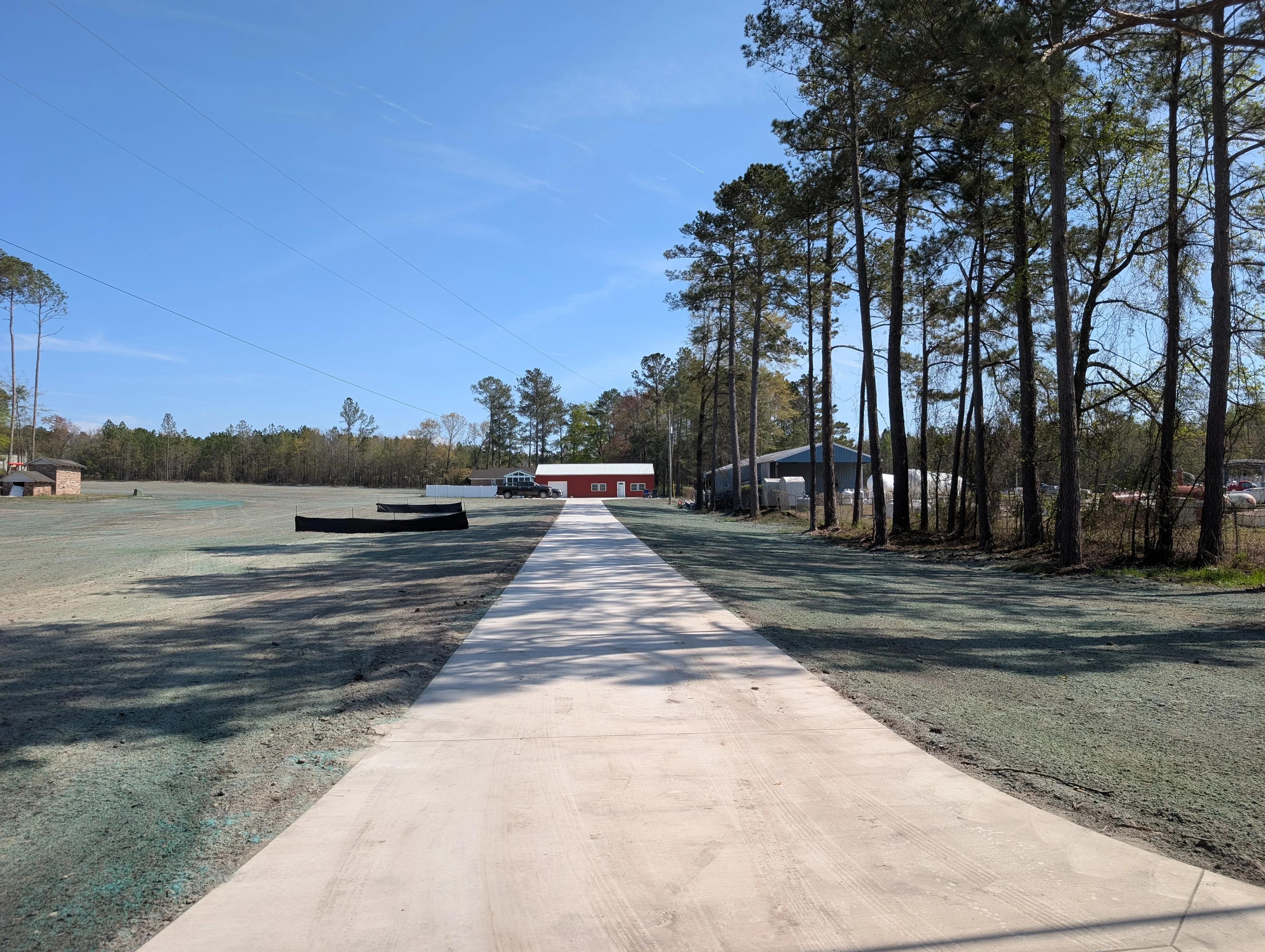 Concrete driveway with graded gravel base and cleared lot surrounded by pine trees