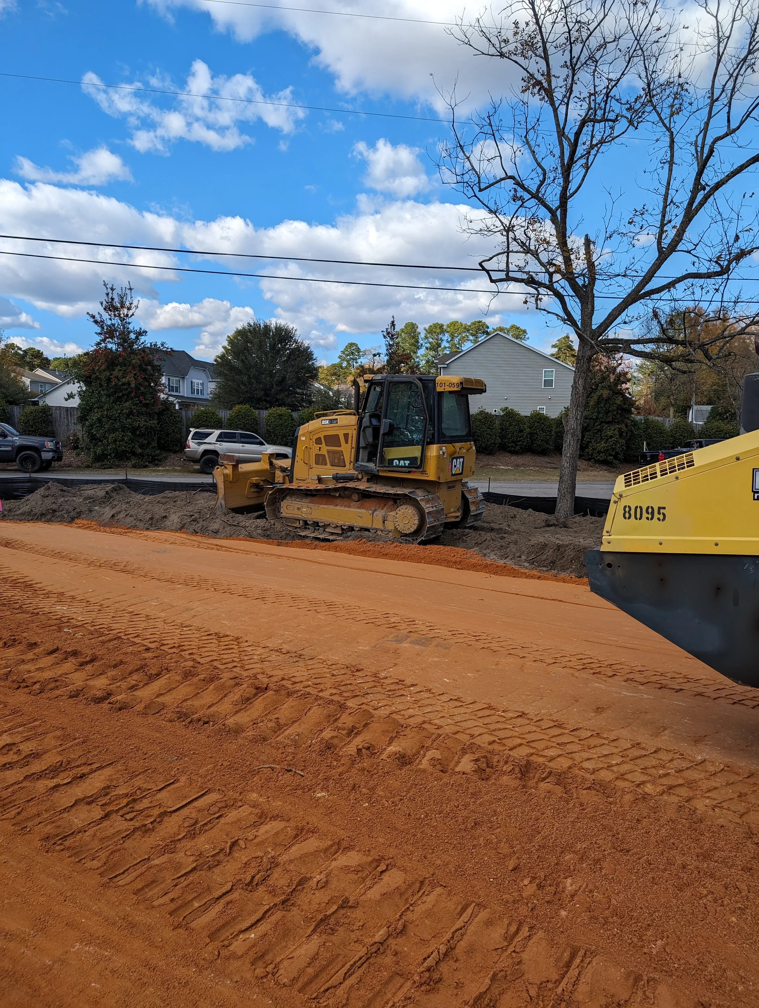 CAT bulldozer grading residential driveway with excavated clay soil and heavy equipment on site
