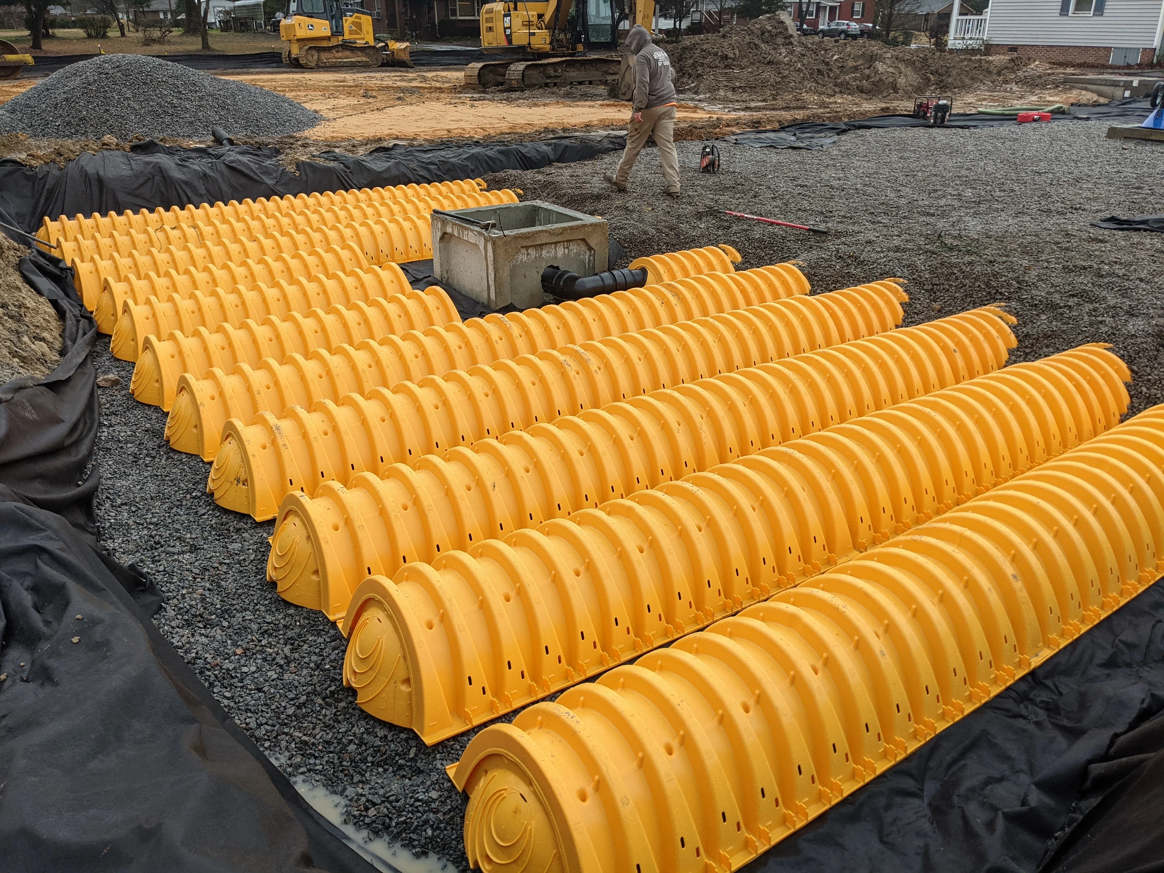 Yellow corrugated drainage pipes laid in parallel rows on gravel base with geotextile fabric and catch basin