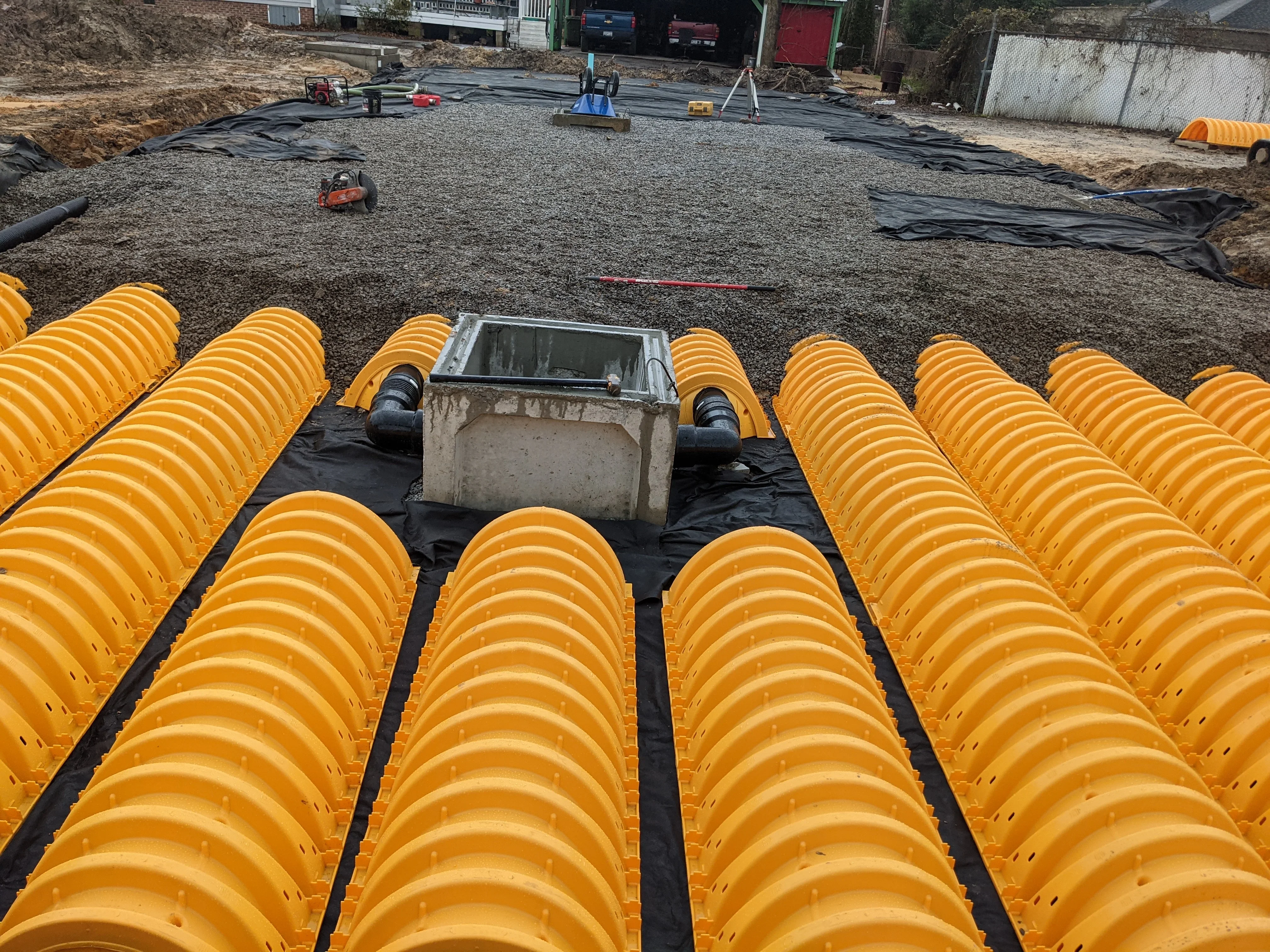 Yellow perforated drain pipes with concrete catch basin on geotextile fabric and gravel base