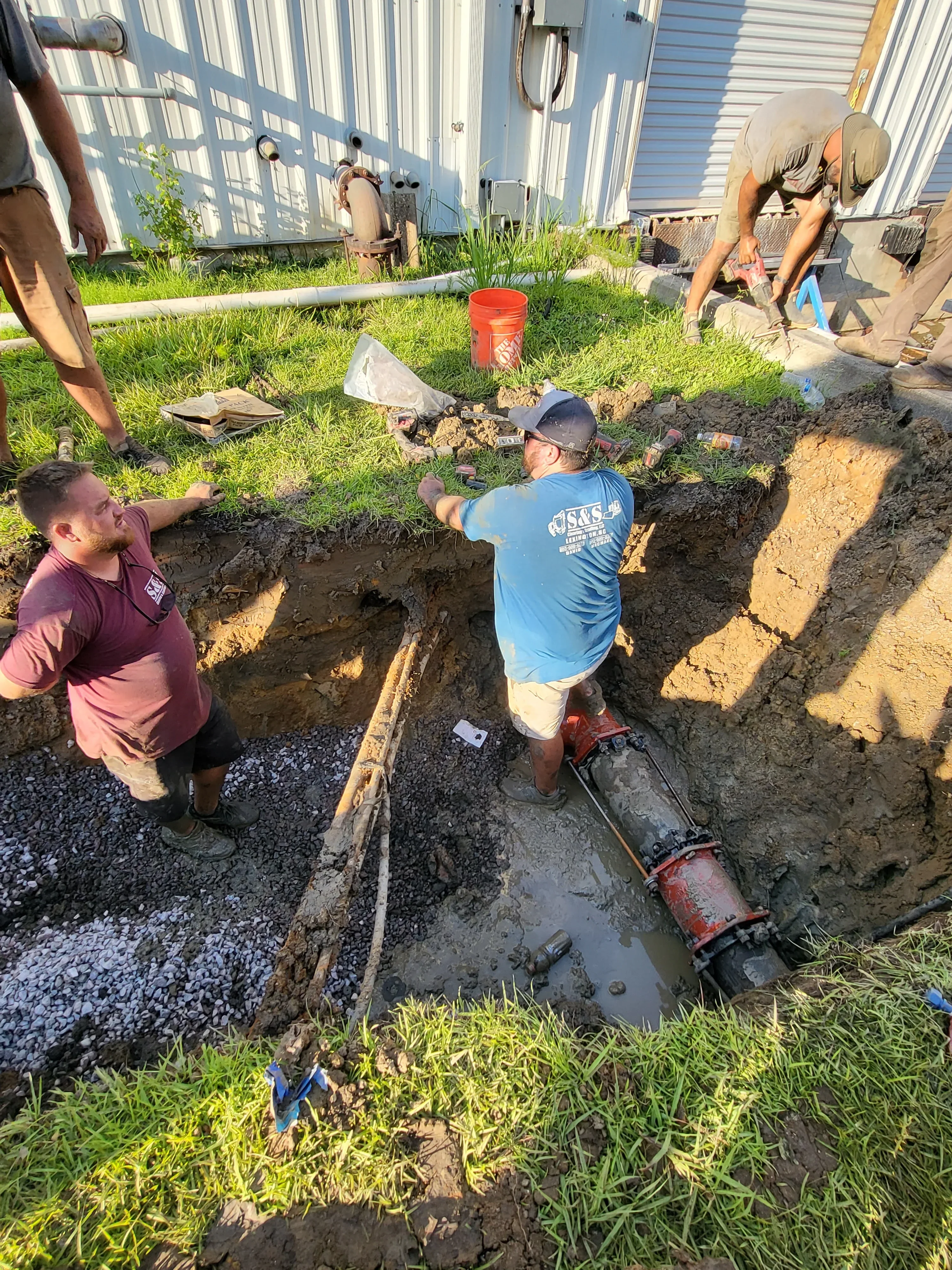 Excavation crew working on utility line trench with gravel base and soil layers exposed