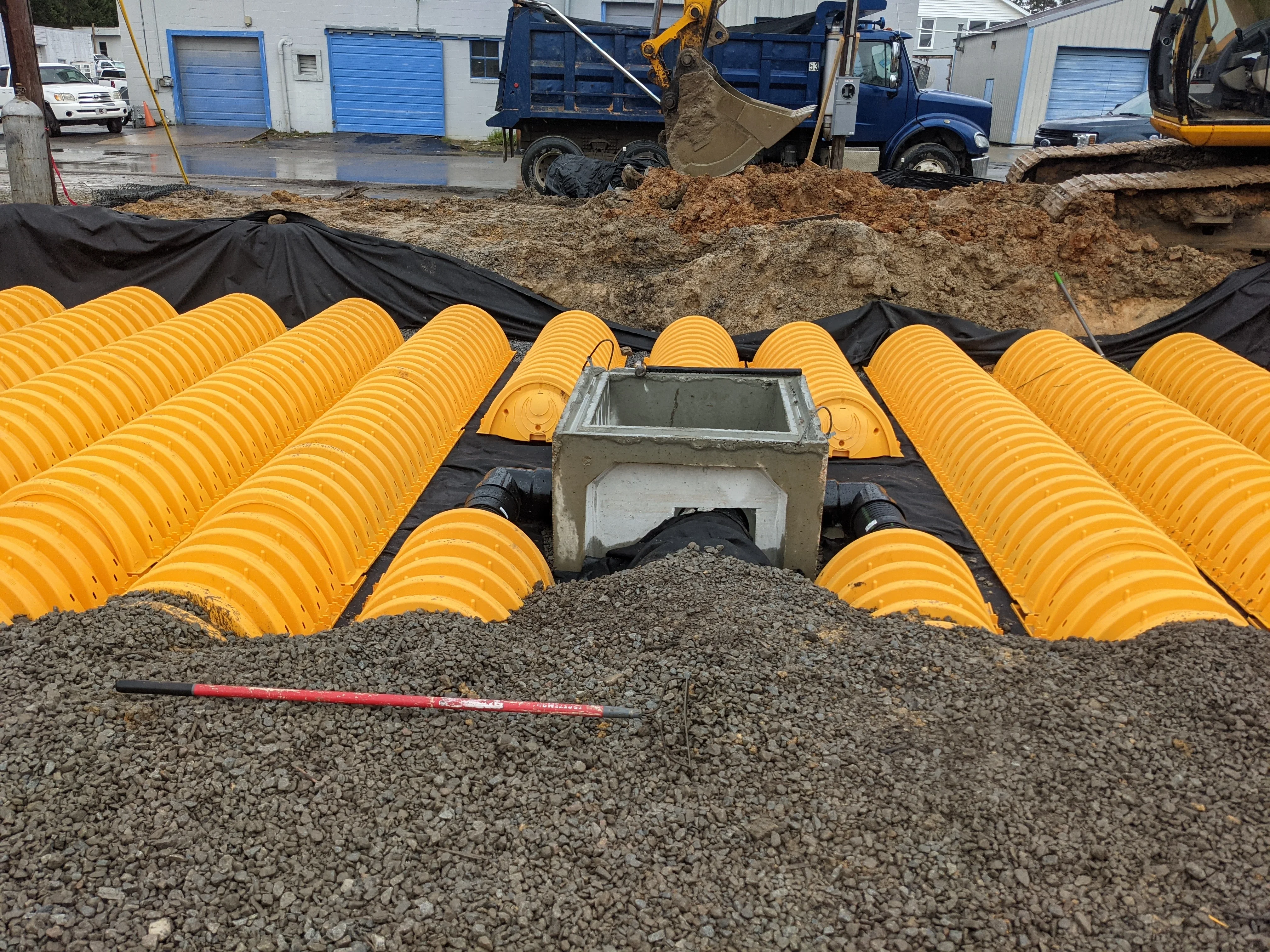 Yellow perforated drainage pipe installation with concrete catch basin and gravel base