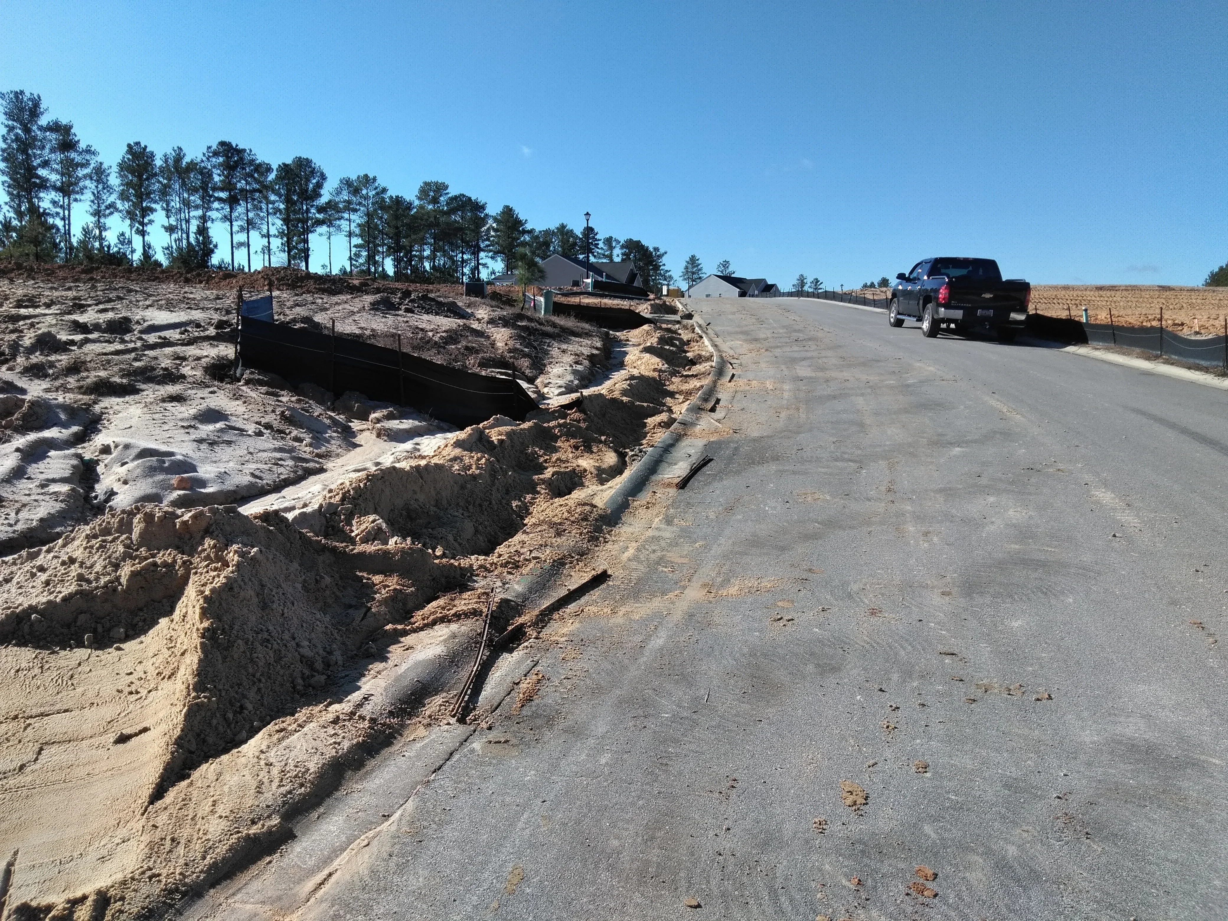 Excavated driveway site with utility trench, graded earth, and new asphalt surface